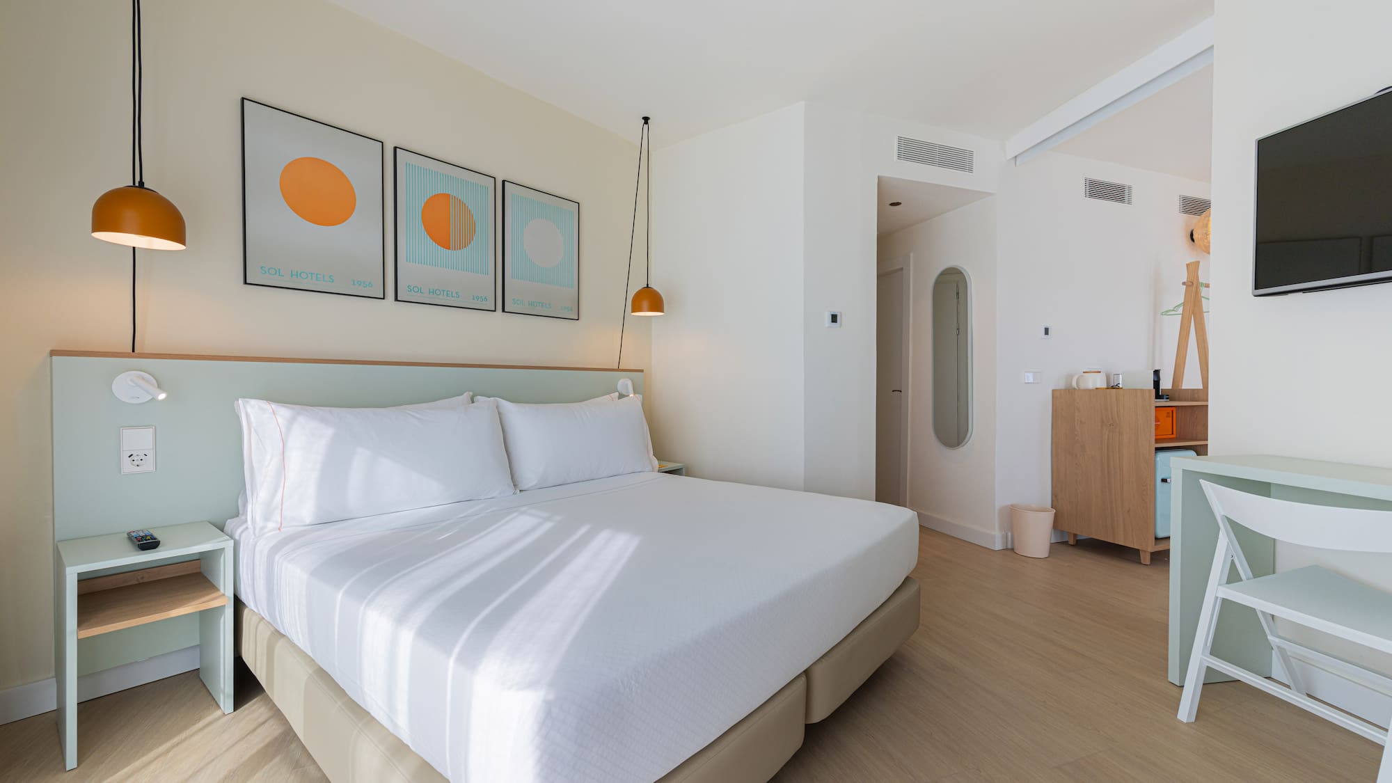 Modern hotel room with white bed, light green headboard, and minimalist art.