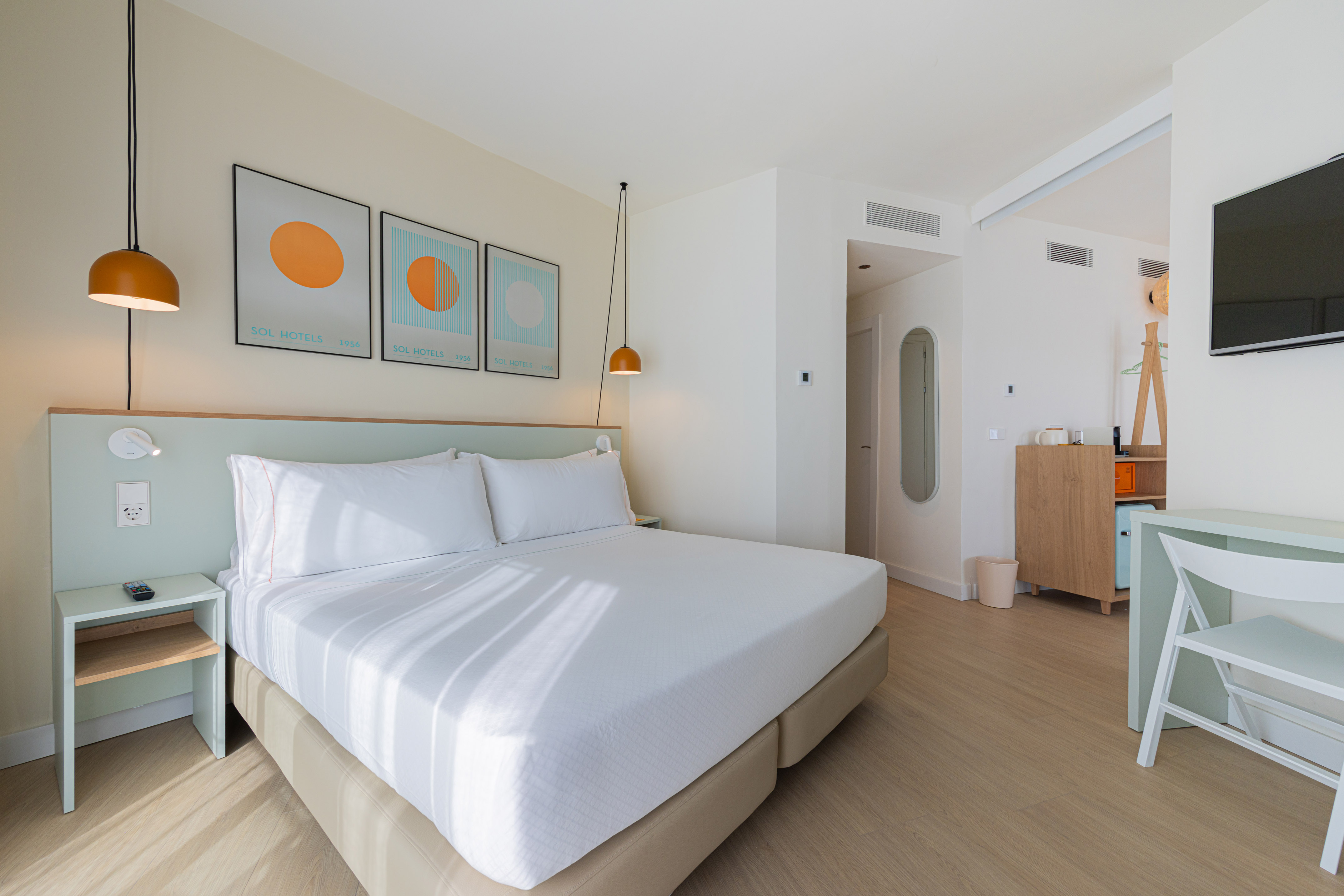Modern hotel room with white bed, light green headboard, and Sol Hotels art.