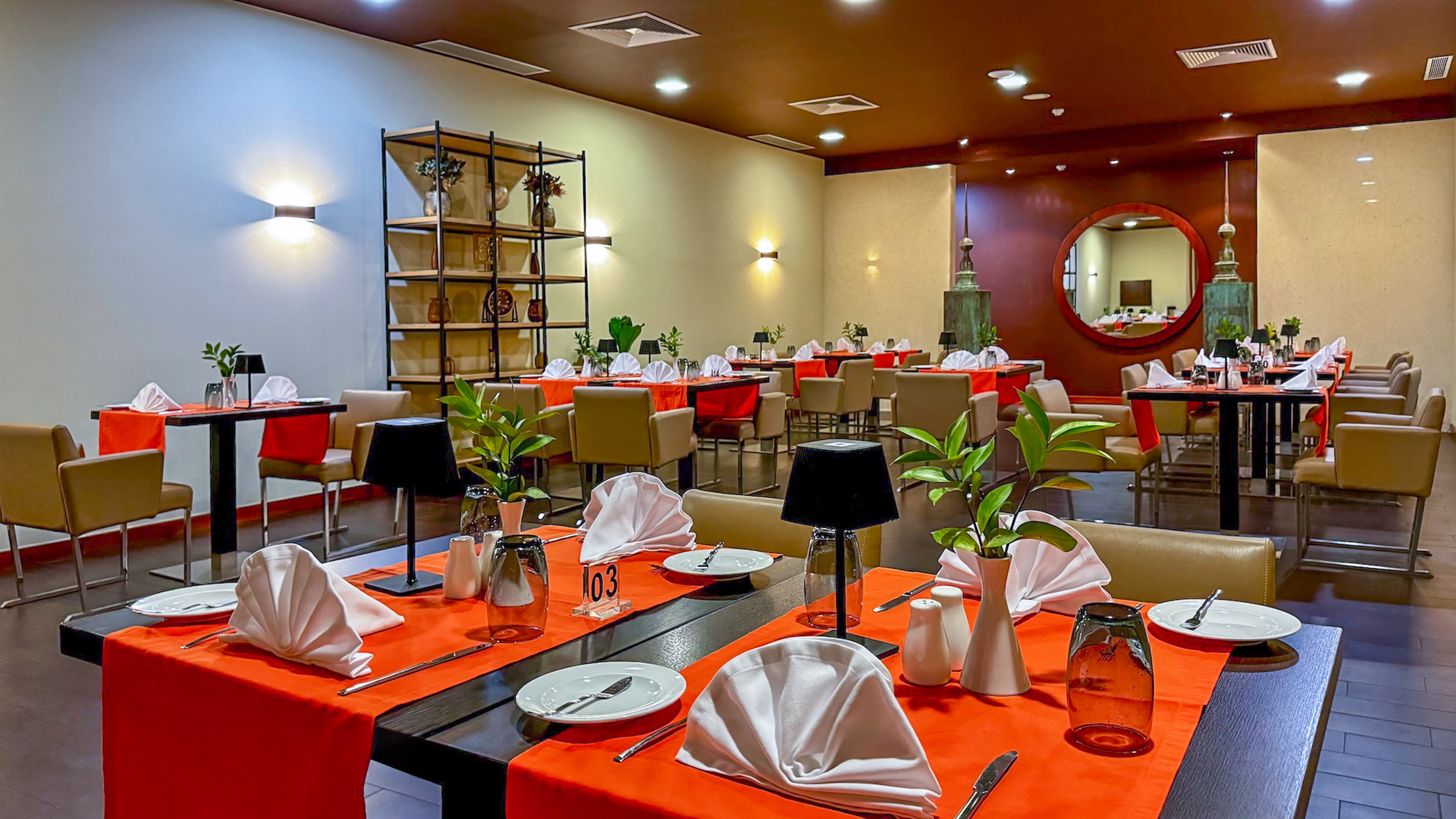 Restaurant dining room with orange table settings and warm ambient lighting.