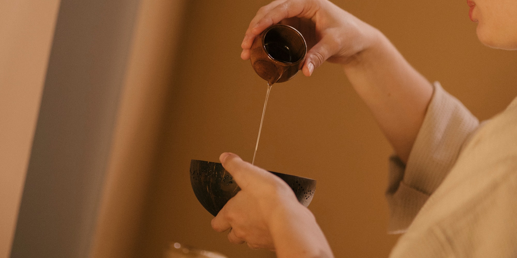 Woman pouring treatment oil into a coconut bowl at a spa.