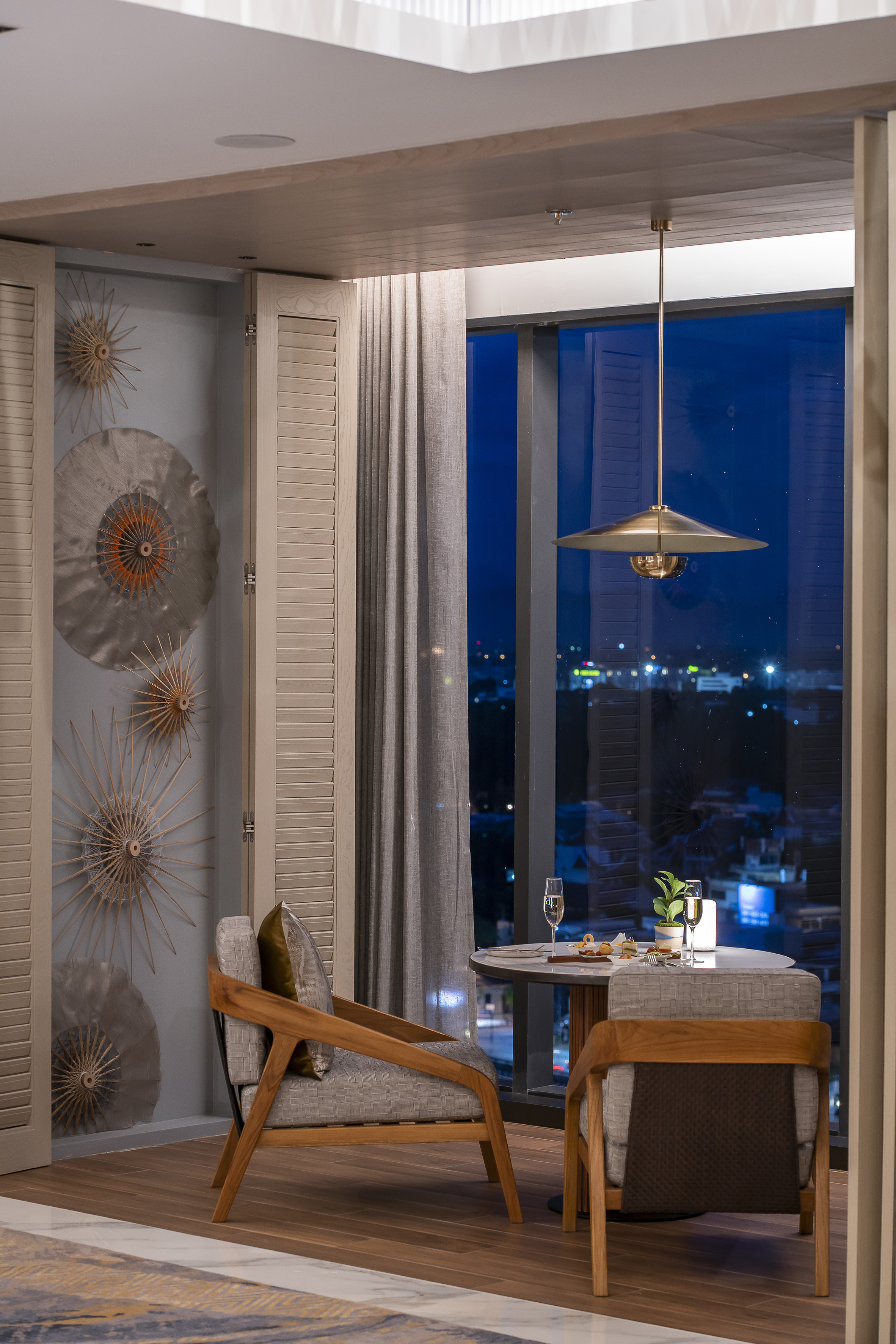 Elegant dining area with city night view, champagne, stylish chairs.