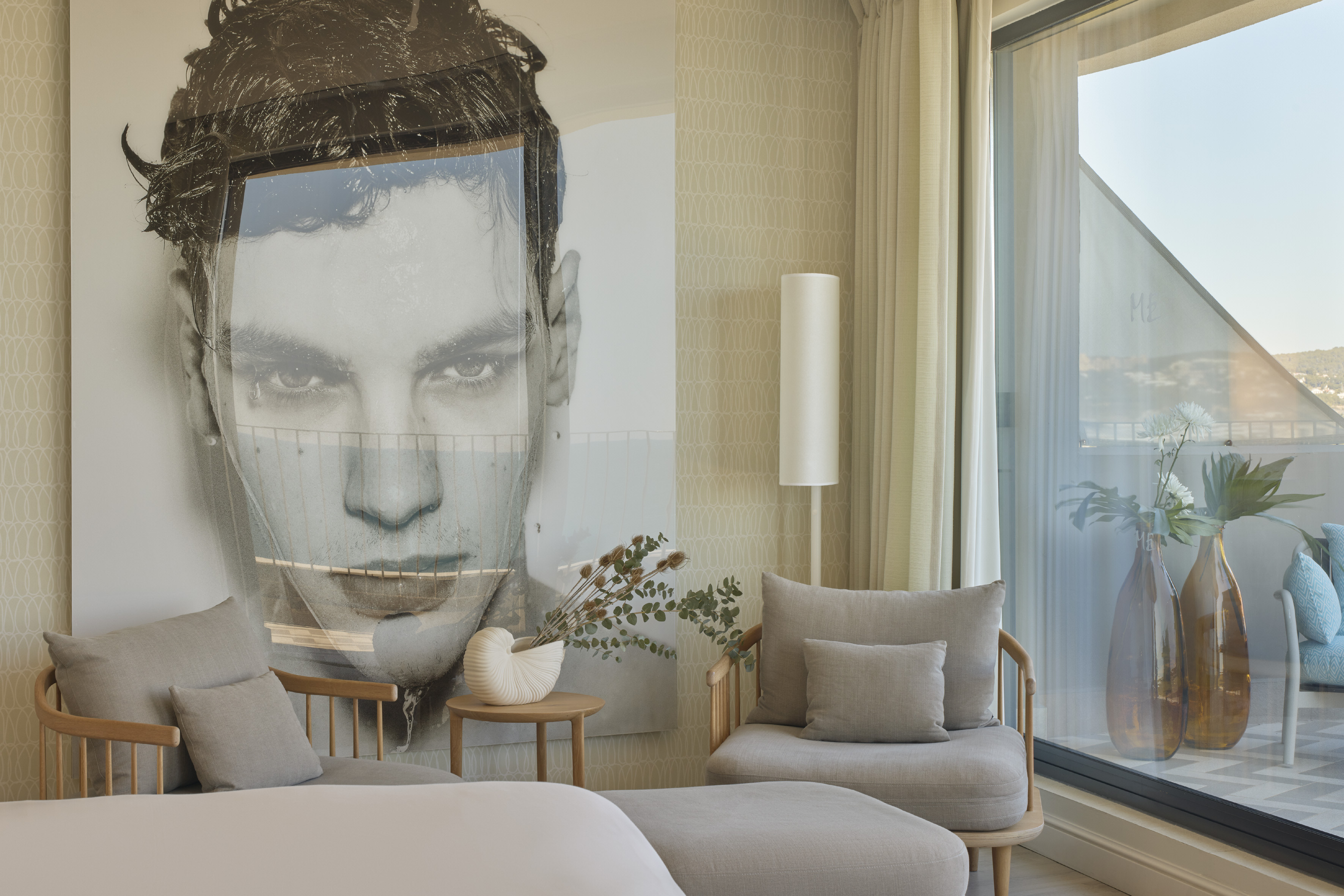 Modern hotel suite with large portrait artwork, neutral seating, and balcony view.