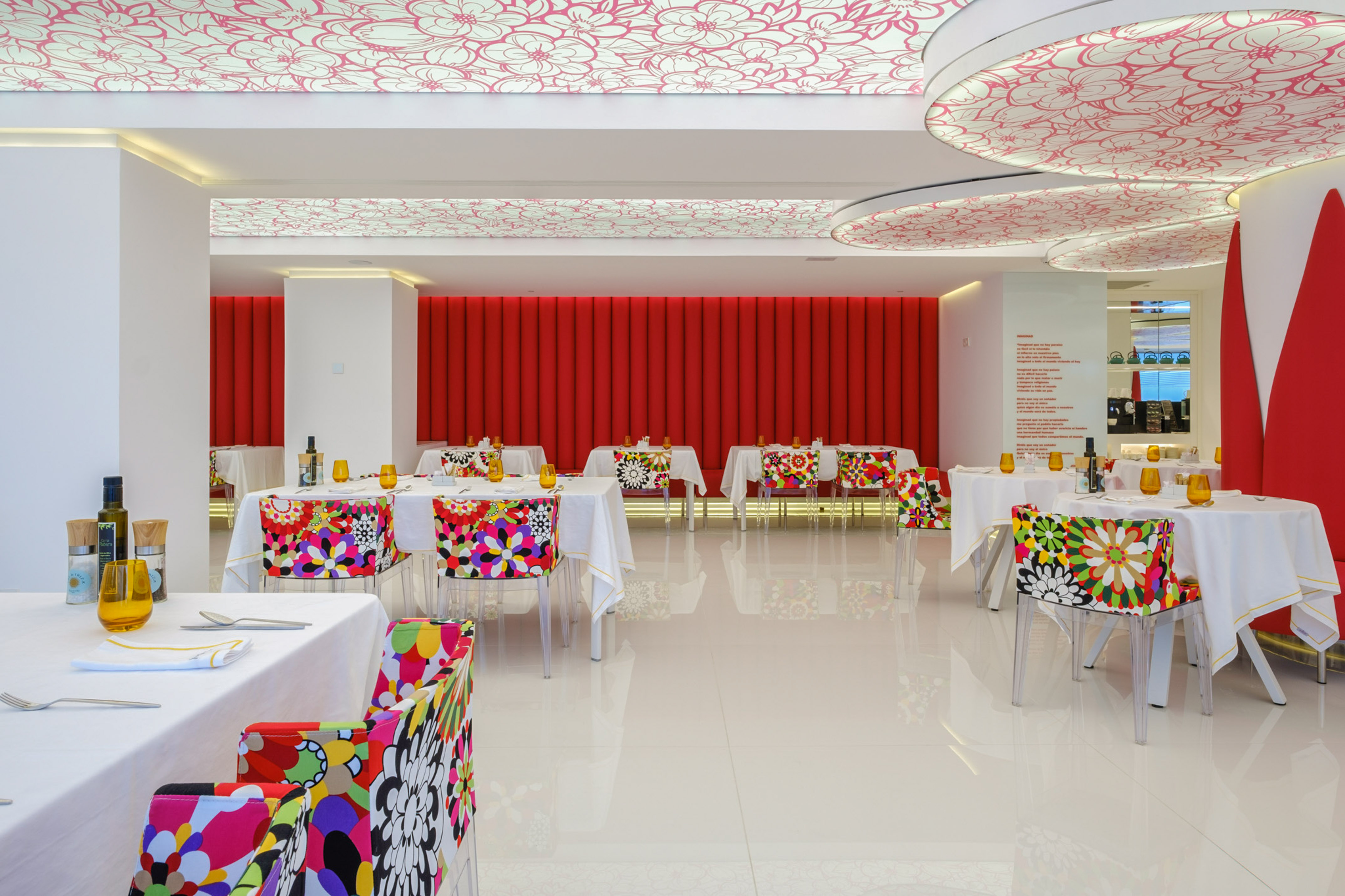 Modern restaurant with vibrant floral chairs, red wall, and patterned ceiling.