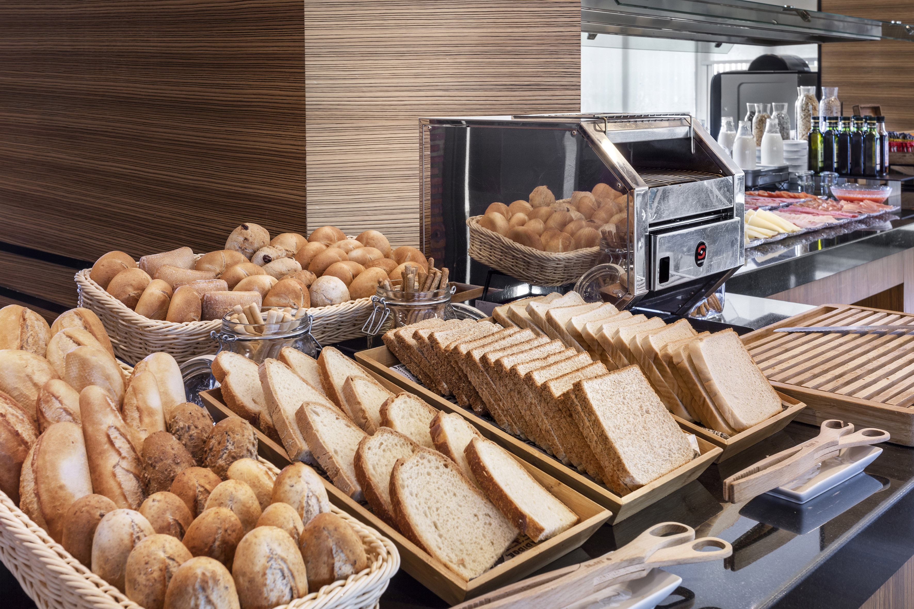 Fresh bread rolls, sliced bread, and toaster at a breakfast buffet.