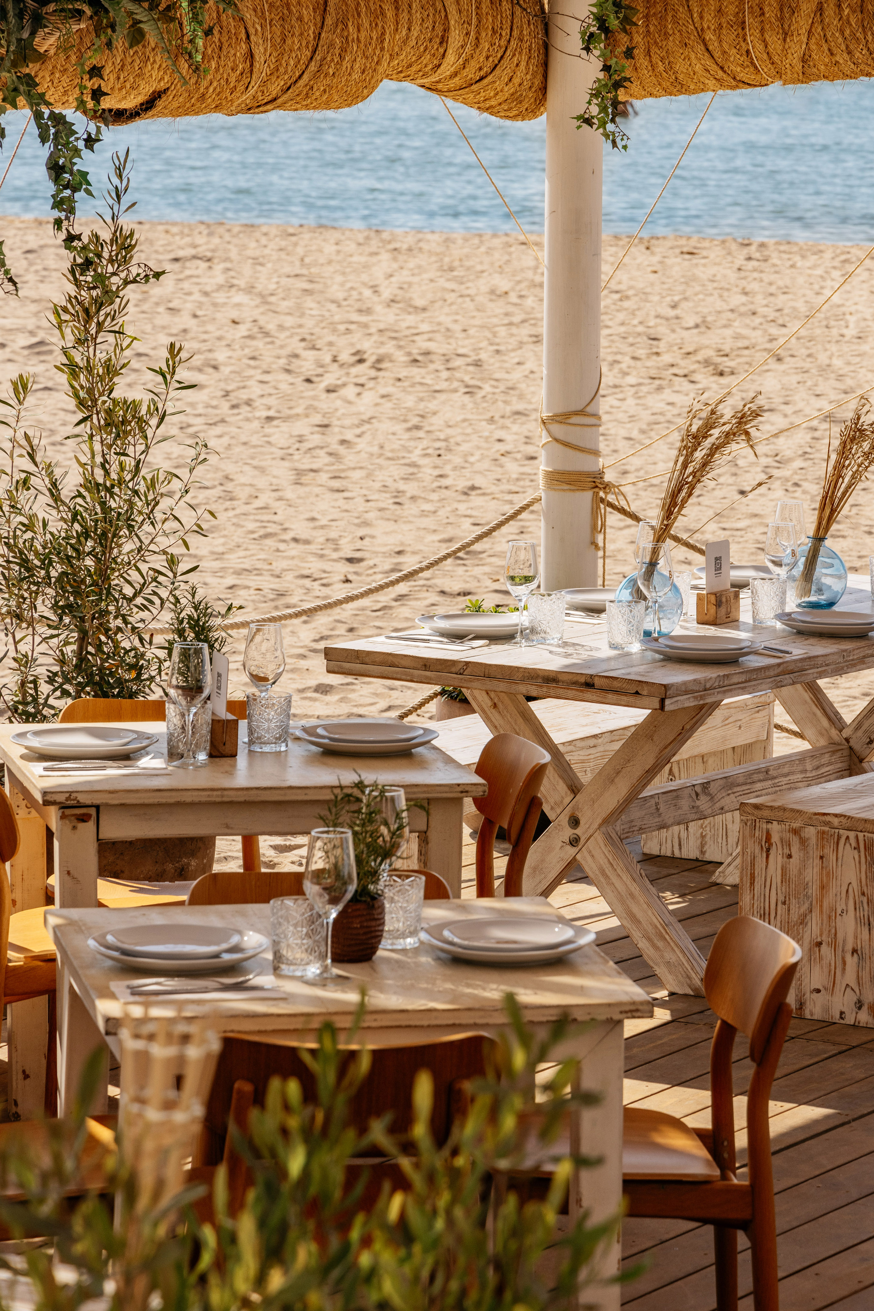 Rustic beach restaurant tables set on a wooden deck overlooking the sea.