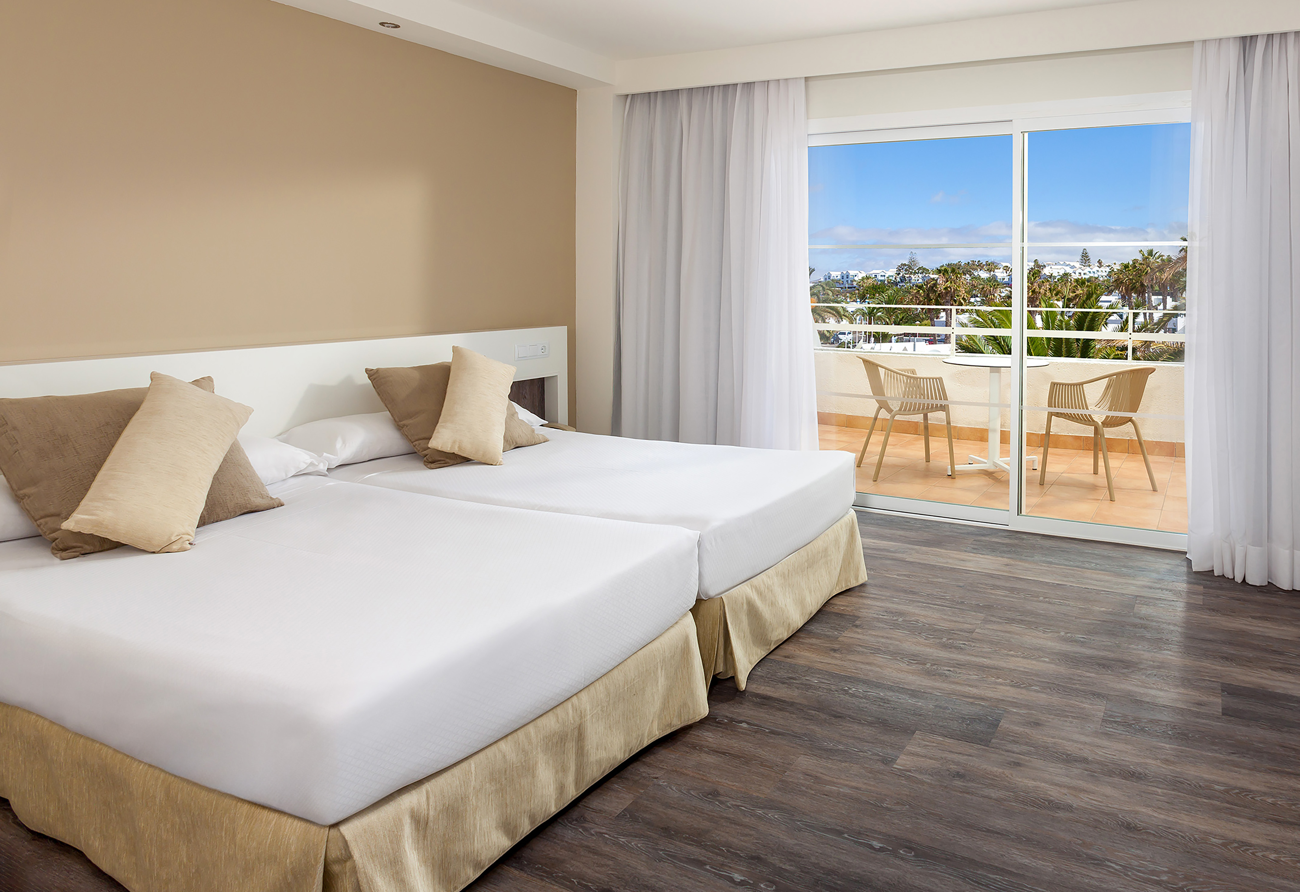 Modern hotel twin room with balcony overlooking tropical resort.
