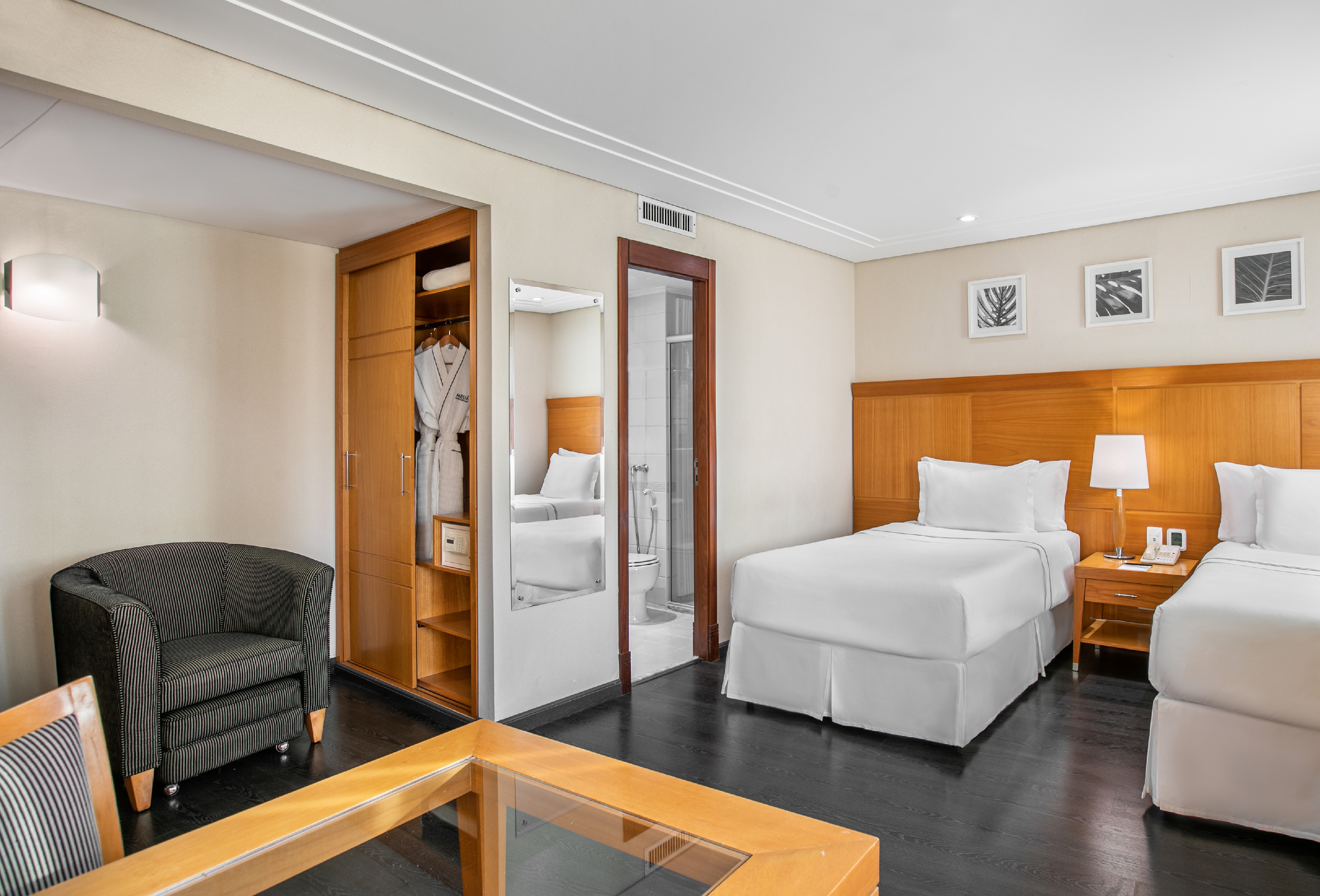 Hotel guest room with twin beds, dark floor, armchair, wardrobe, and bathroom.