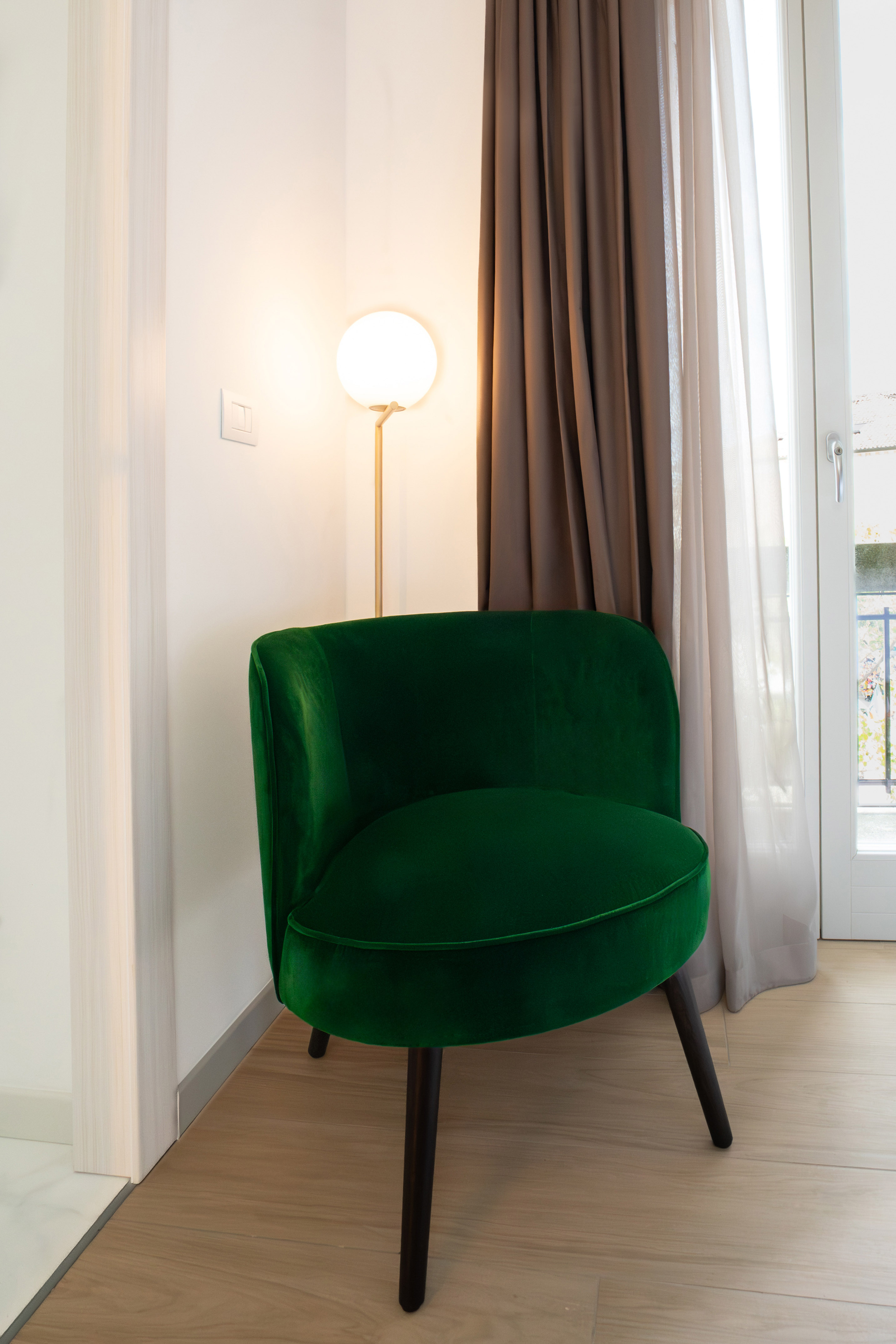 Modern green velvet accent chair beside a floor lamp and sheer curtains.