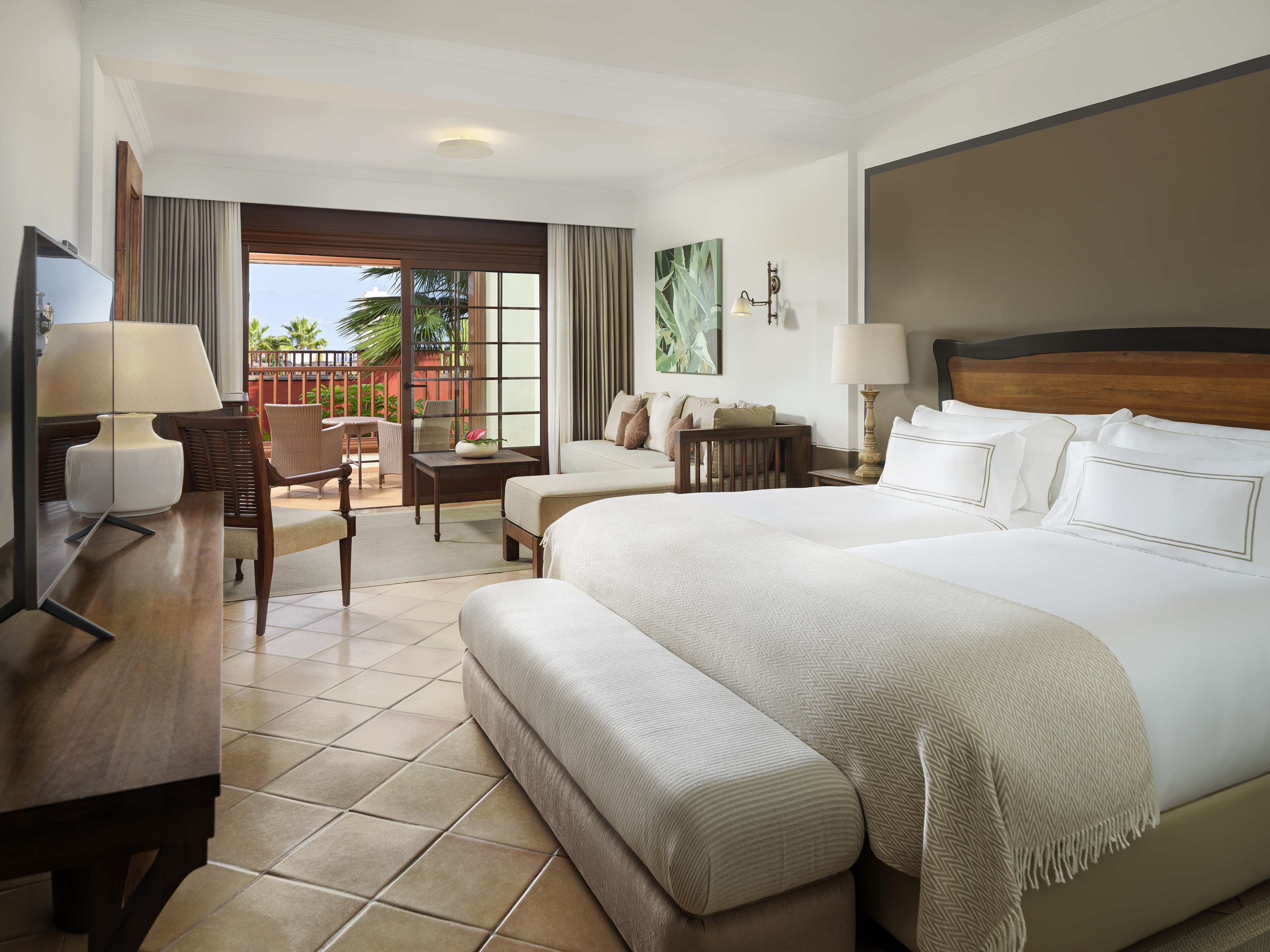 Luxury hotel suite with king bed, balcony, and tropical palm views.