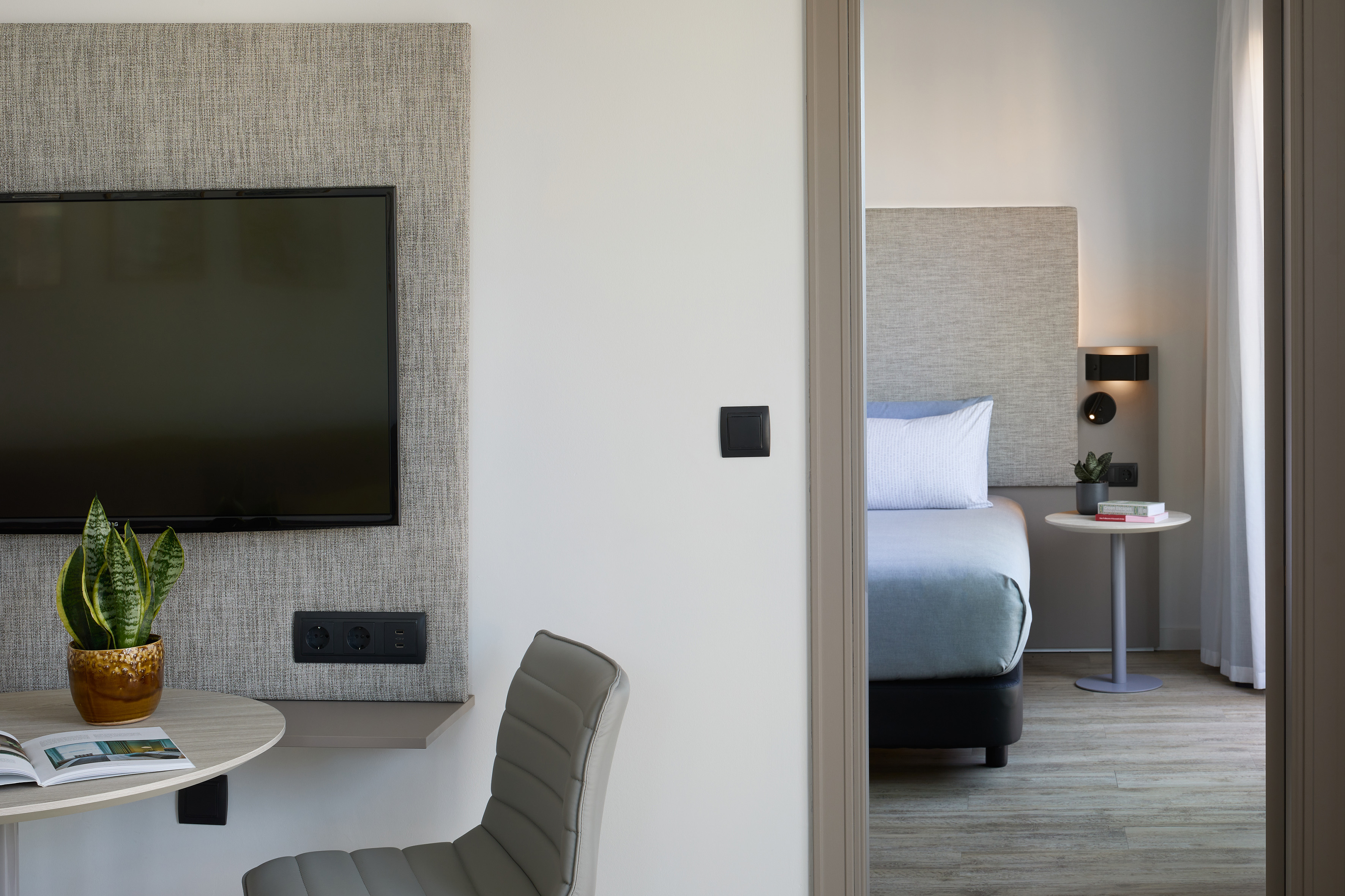 Modern hotel room interior with TV, desk, and adjacent bedroom view.