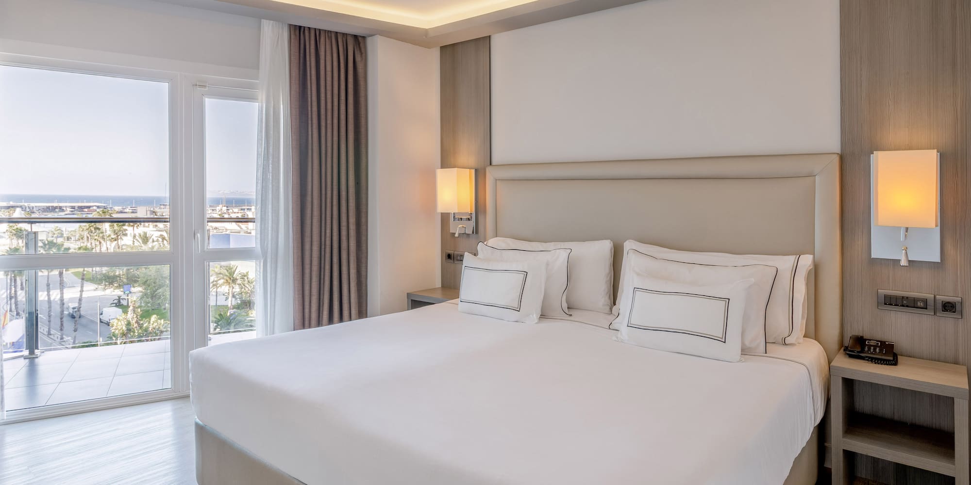 Habitación de hotel moderna con cama king, balcón y vista al mar.
