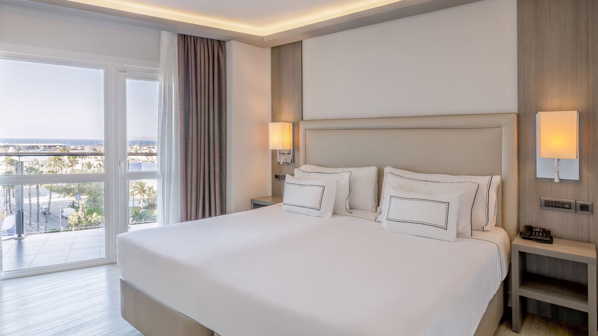 Habitación de hotel moderna con cama king, balcón y vista al mar.