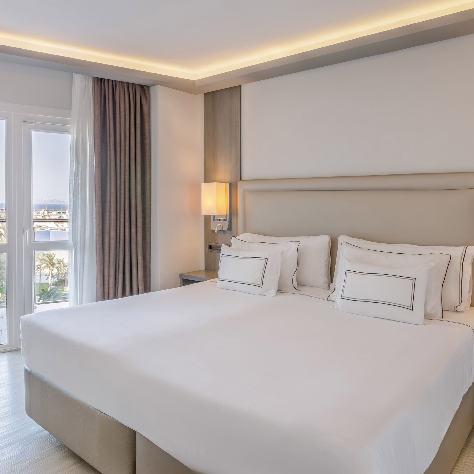 Habitación de hotel moderna con cama king, balcón y vista al mar.