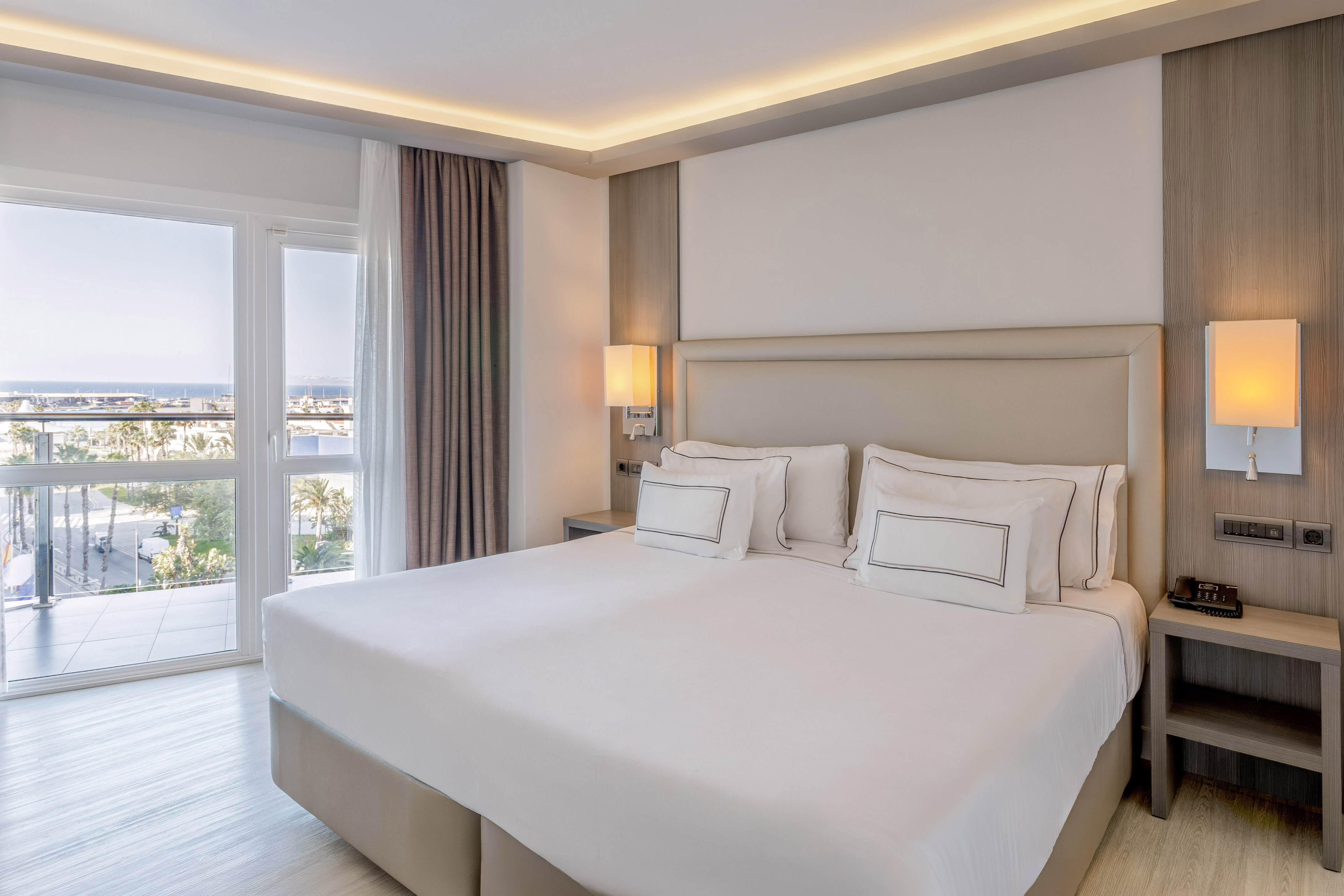 Habitación de hotel moderna con cama king, balcón y vista al mar.