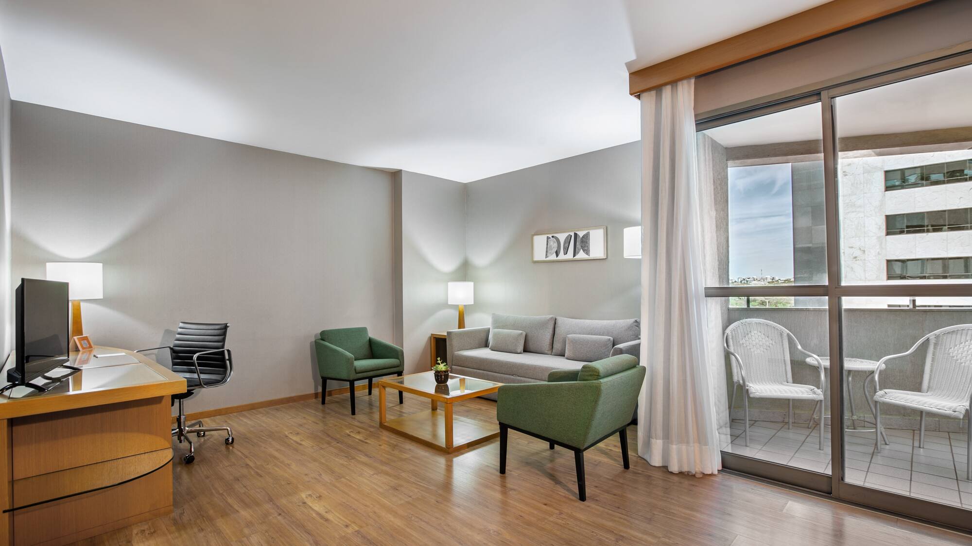 Modern hotel suite living room with gray sofa, green chairs, desk, and balcony.
