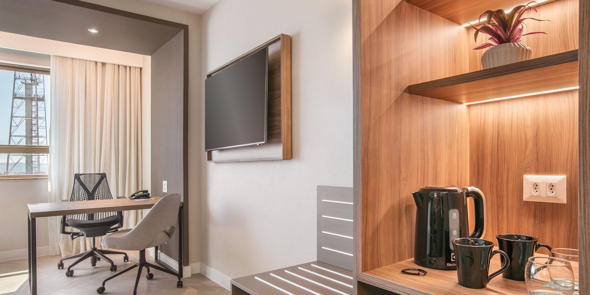 Modern hotel room with workspace, TV, and illuminated coffee/tea station.
