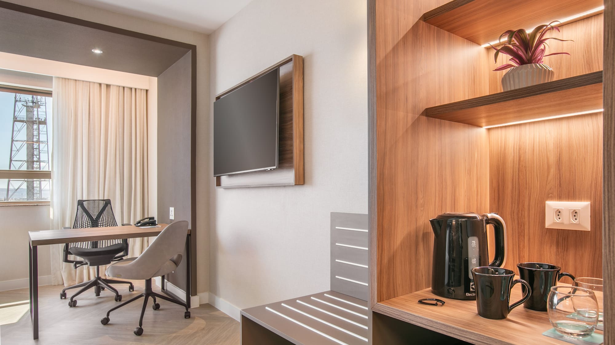 Modern hotel room with workspace, wall TV, and beverage station.