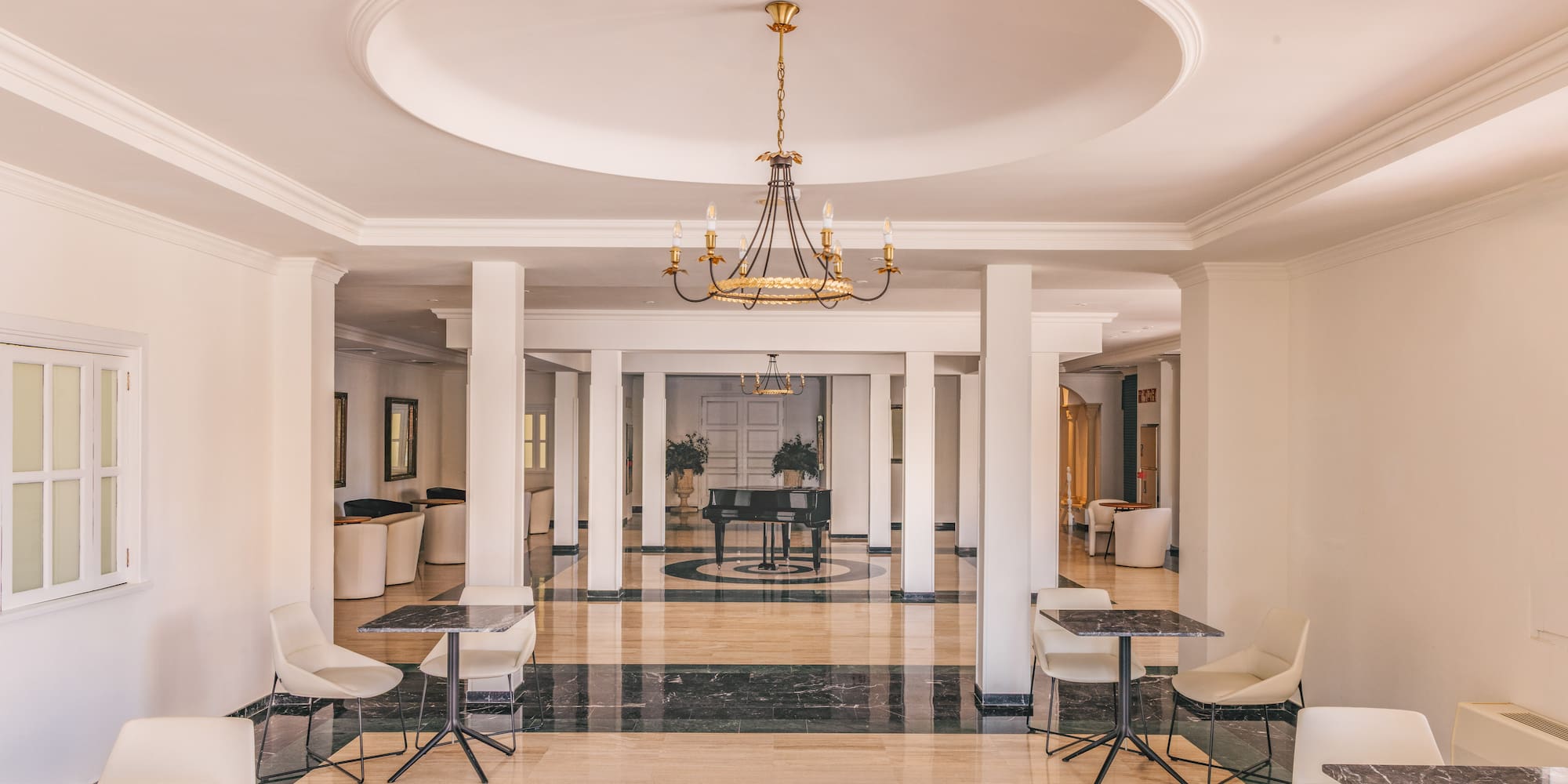 Elegant hotel lobby with marble floor, chandelier, columns, and a grand piano.