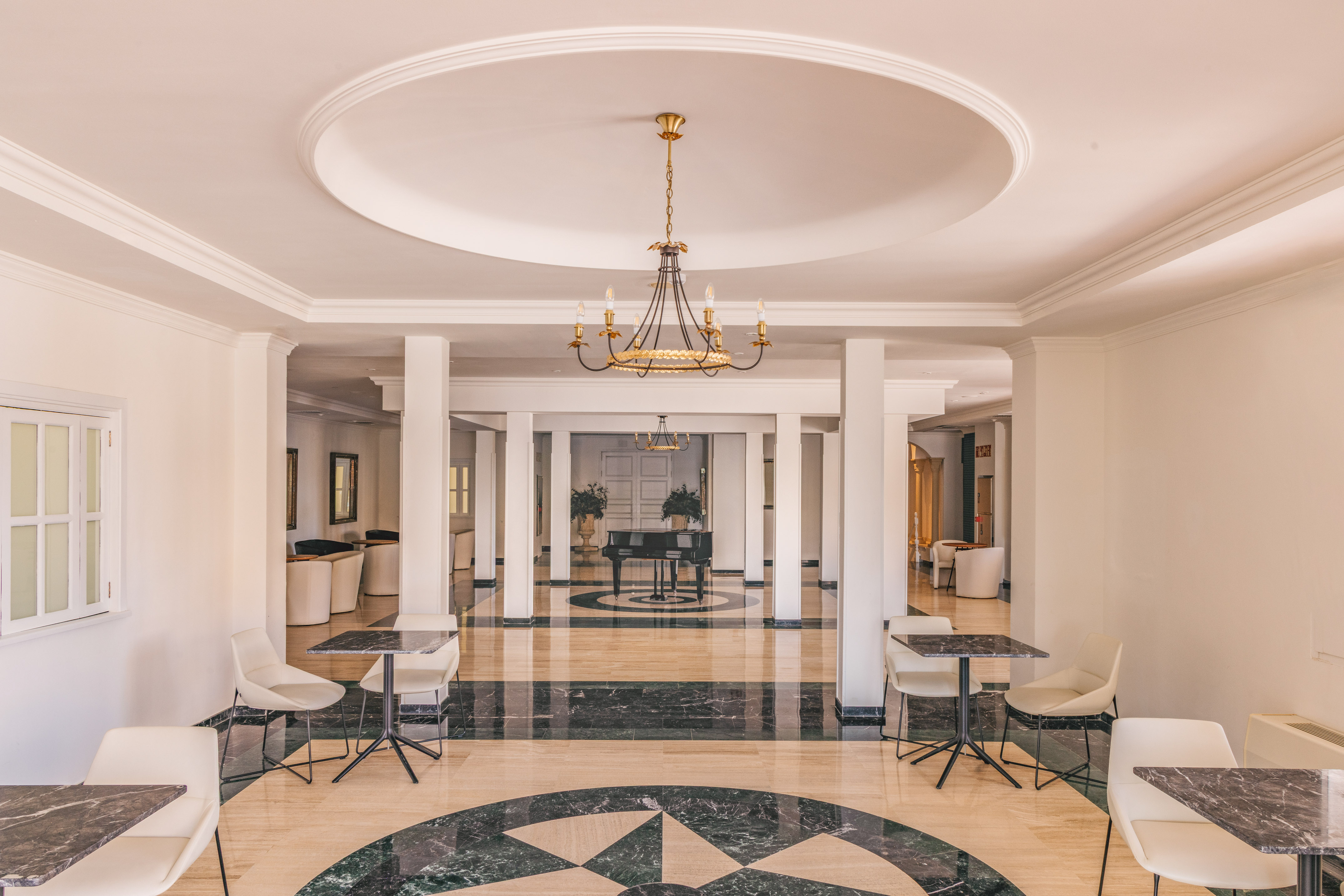 Elegant hotel lobby with marble floor, chandelier, columns, and a grand piano.
