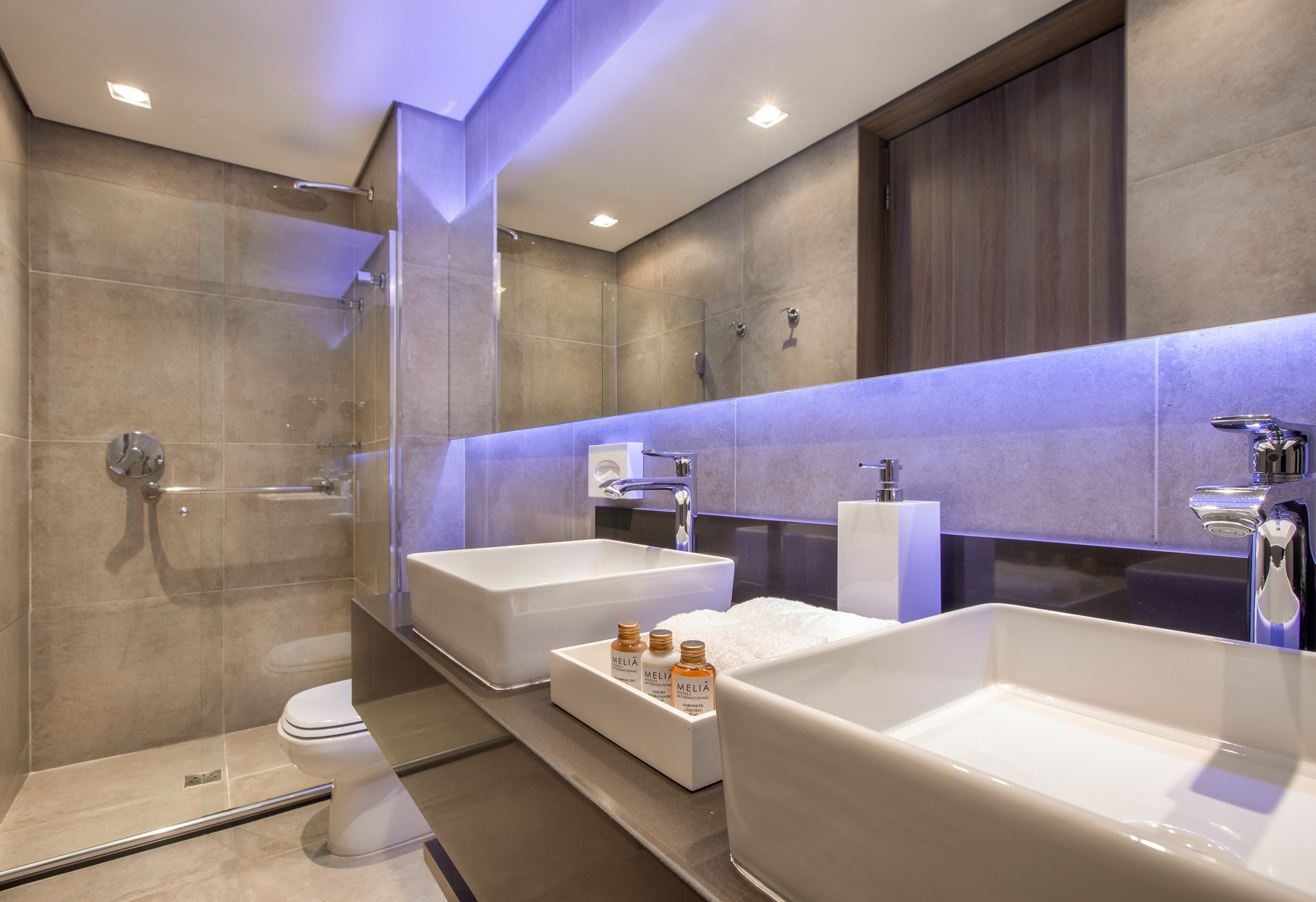 Modern Meliá hotel bathroom with dual sinks, blue LED mirror, and shower.