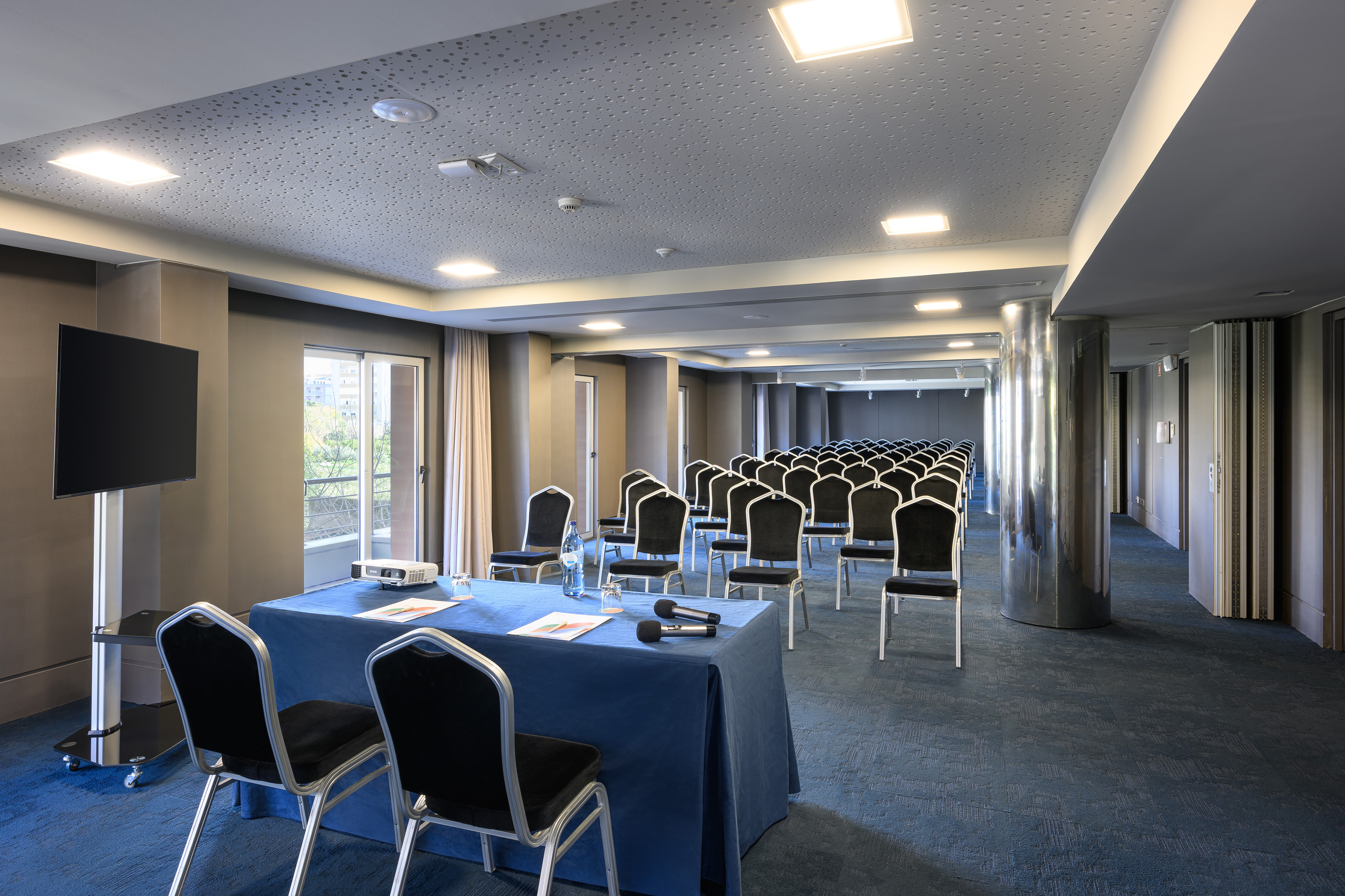 Modern conference room with rows of chairs, blue table, projector, and screen.