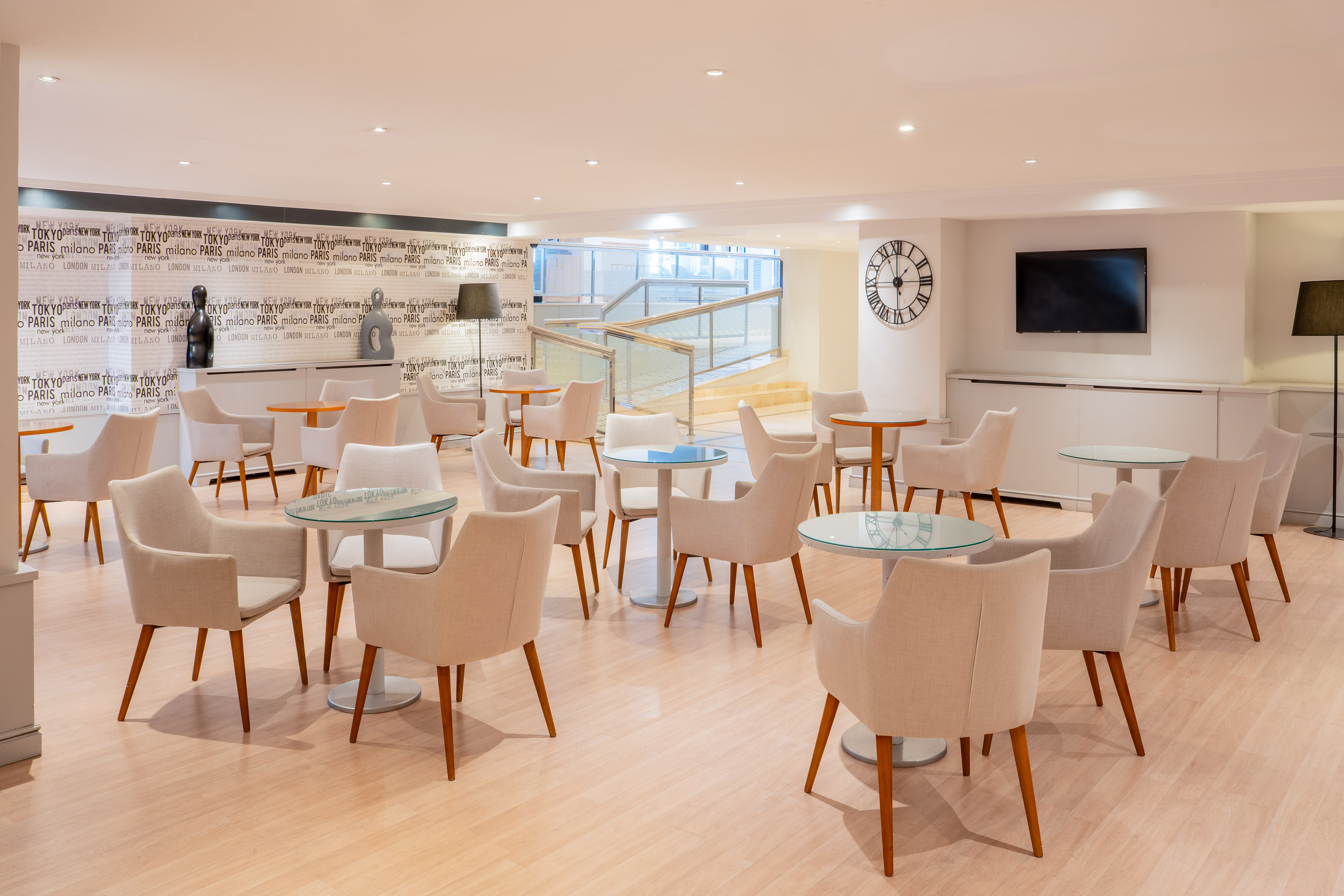 Bright hotel lobby lounge with modern chairs, small tables, and city wallpaper.