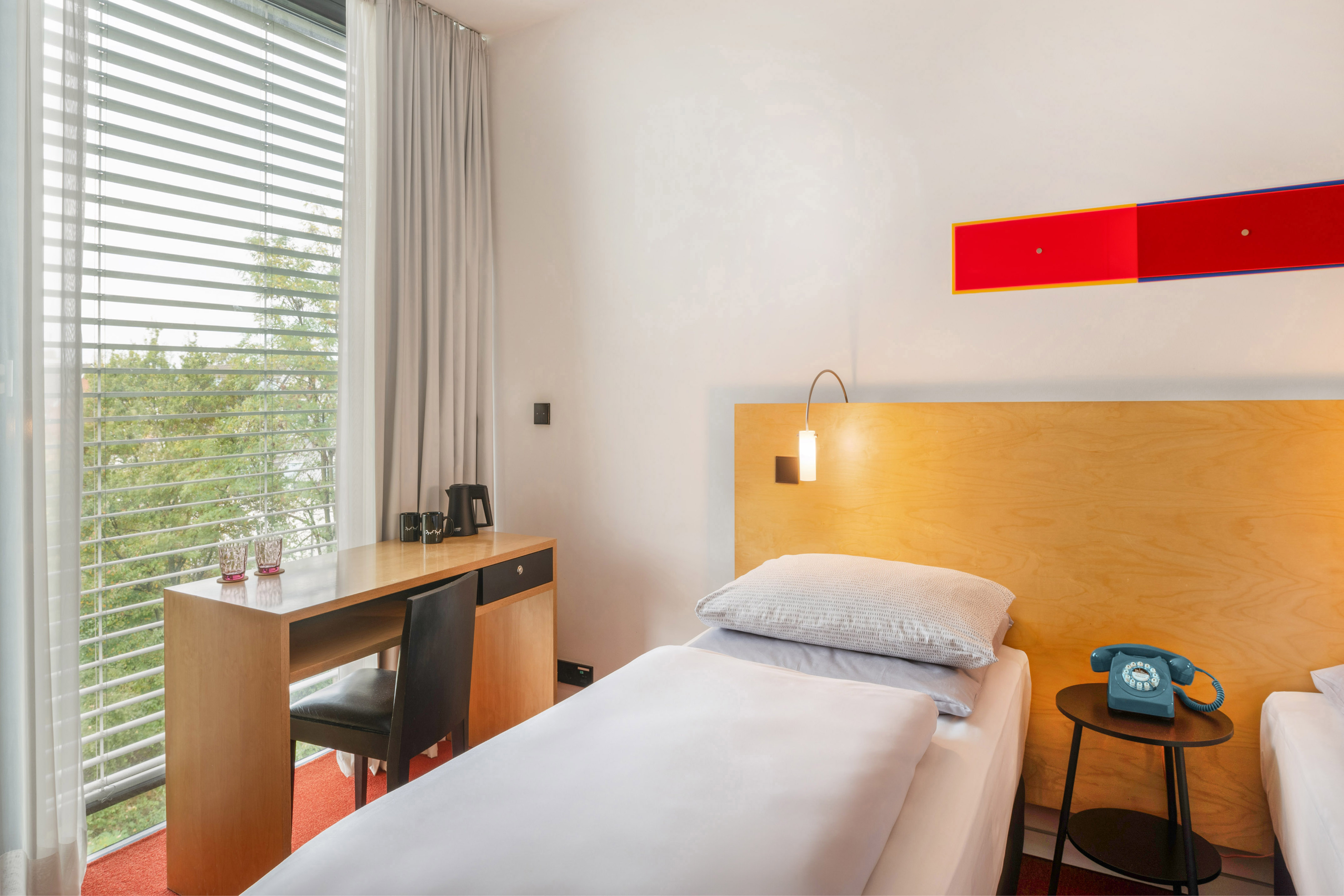 Modern hotel room with single bed, desk, window view, and retro blue telephone. - The INNSiDE Twin Room - INNSiDE Düsseldorf Seestern, Düsseldorf