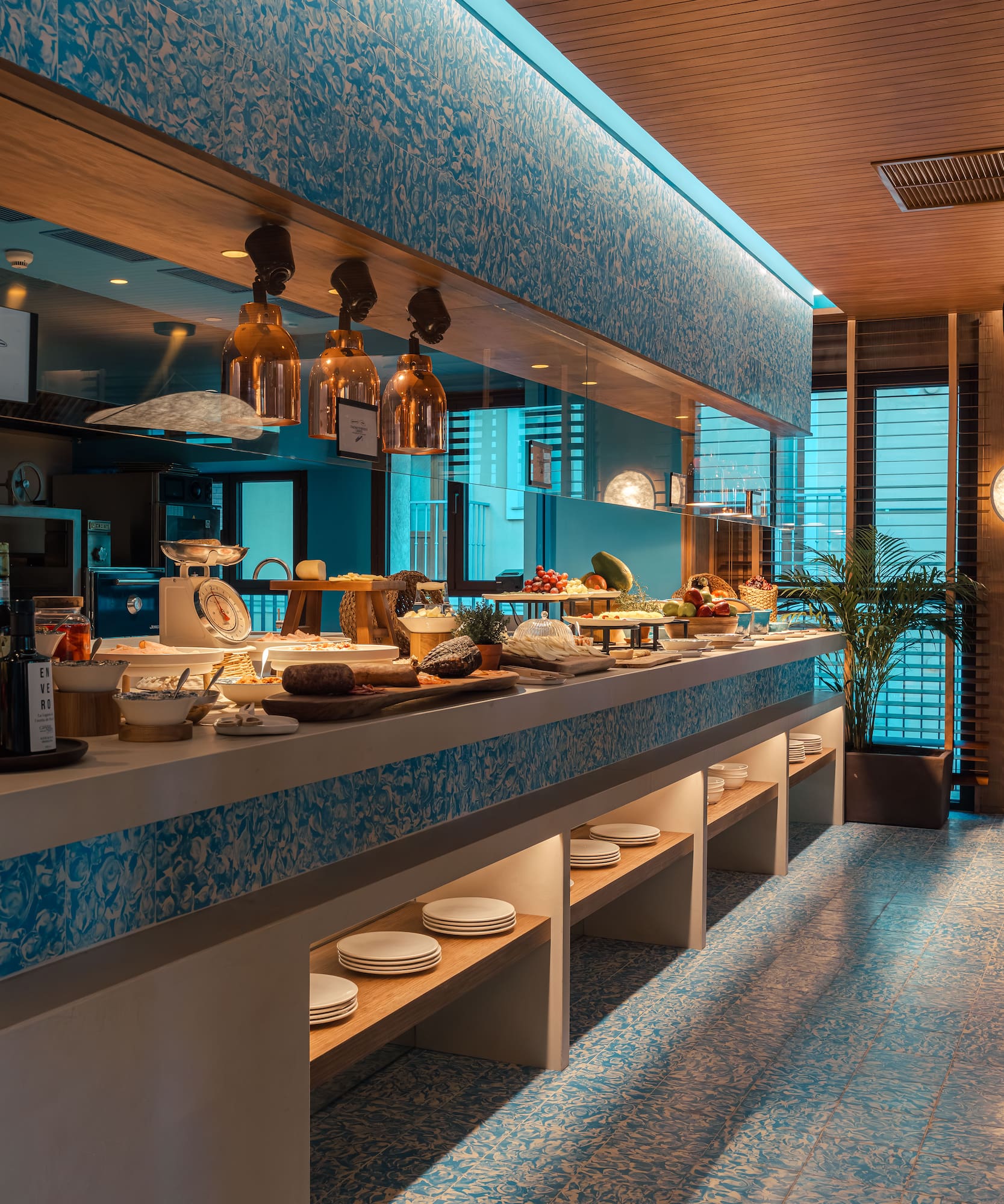 Modern breakfast buffet with fresh food, blue patterned tiles, and copper lighting.