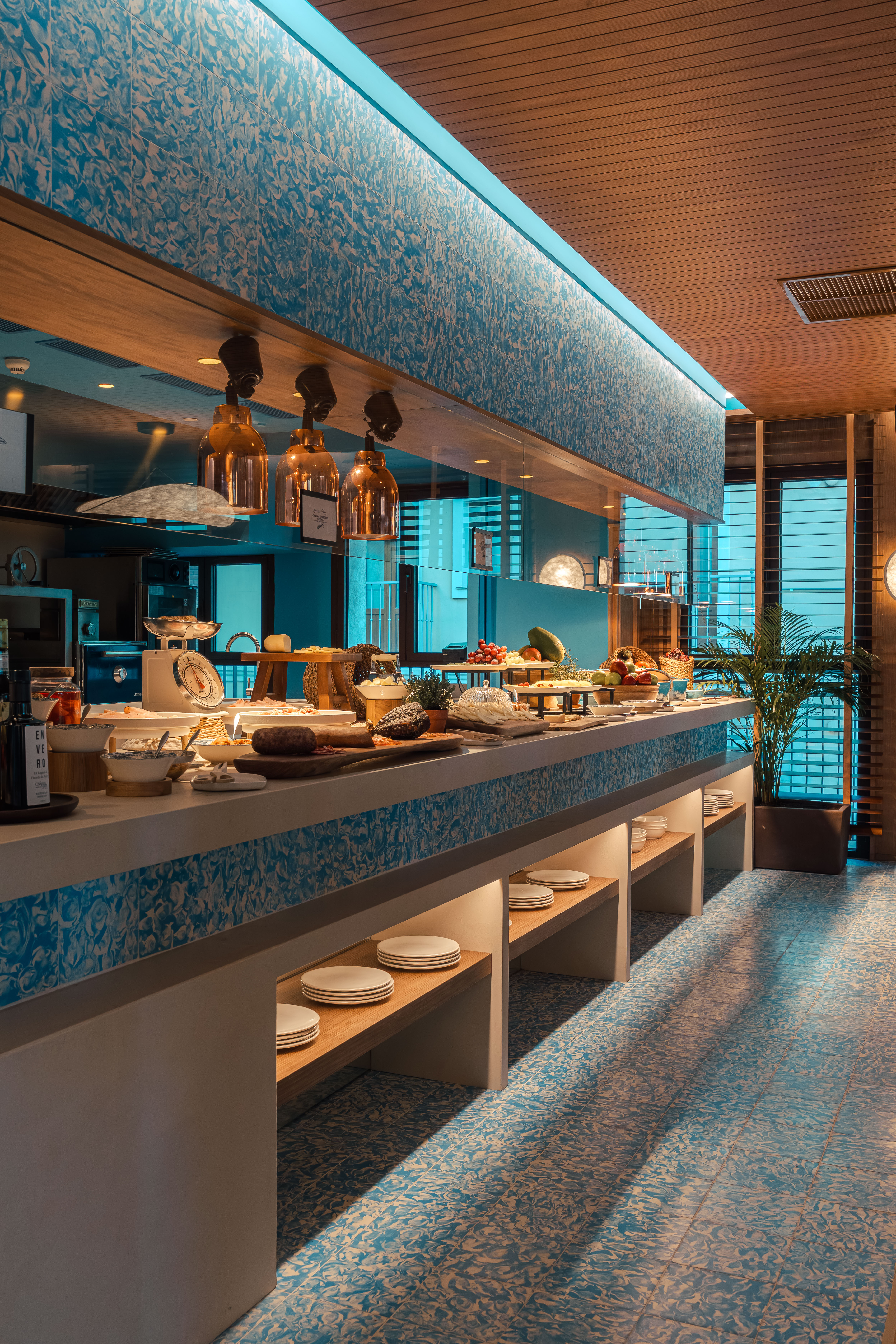 Modern breakfast buffet with fresh food, blue patterned tiles, and copper lighting.