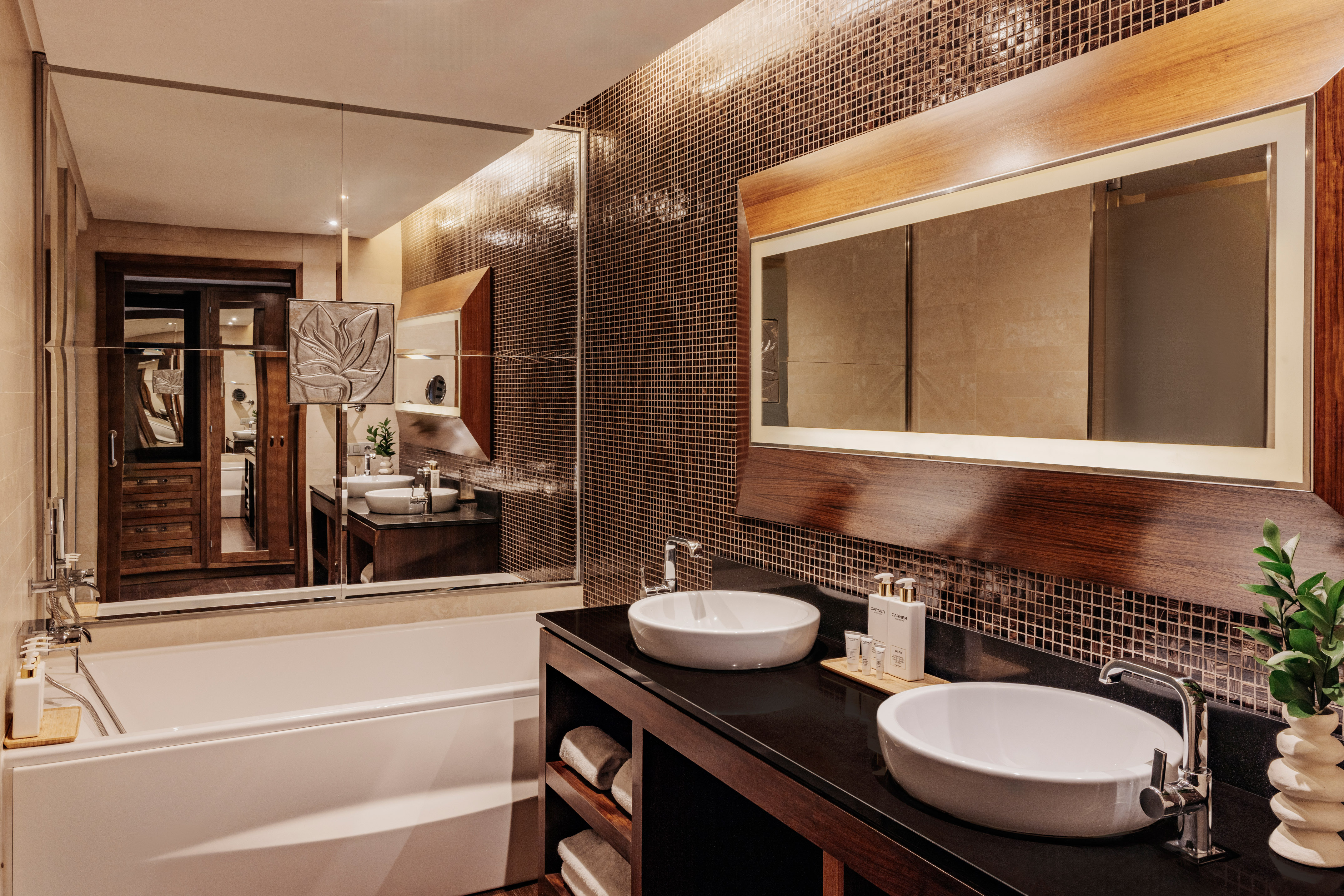 Modern bathroom with white tub, double vessel sinks, dark vanity, mosaic wall.