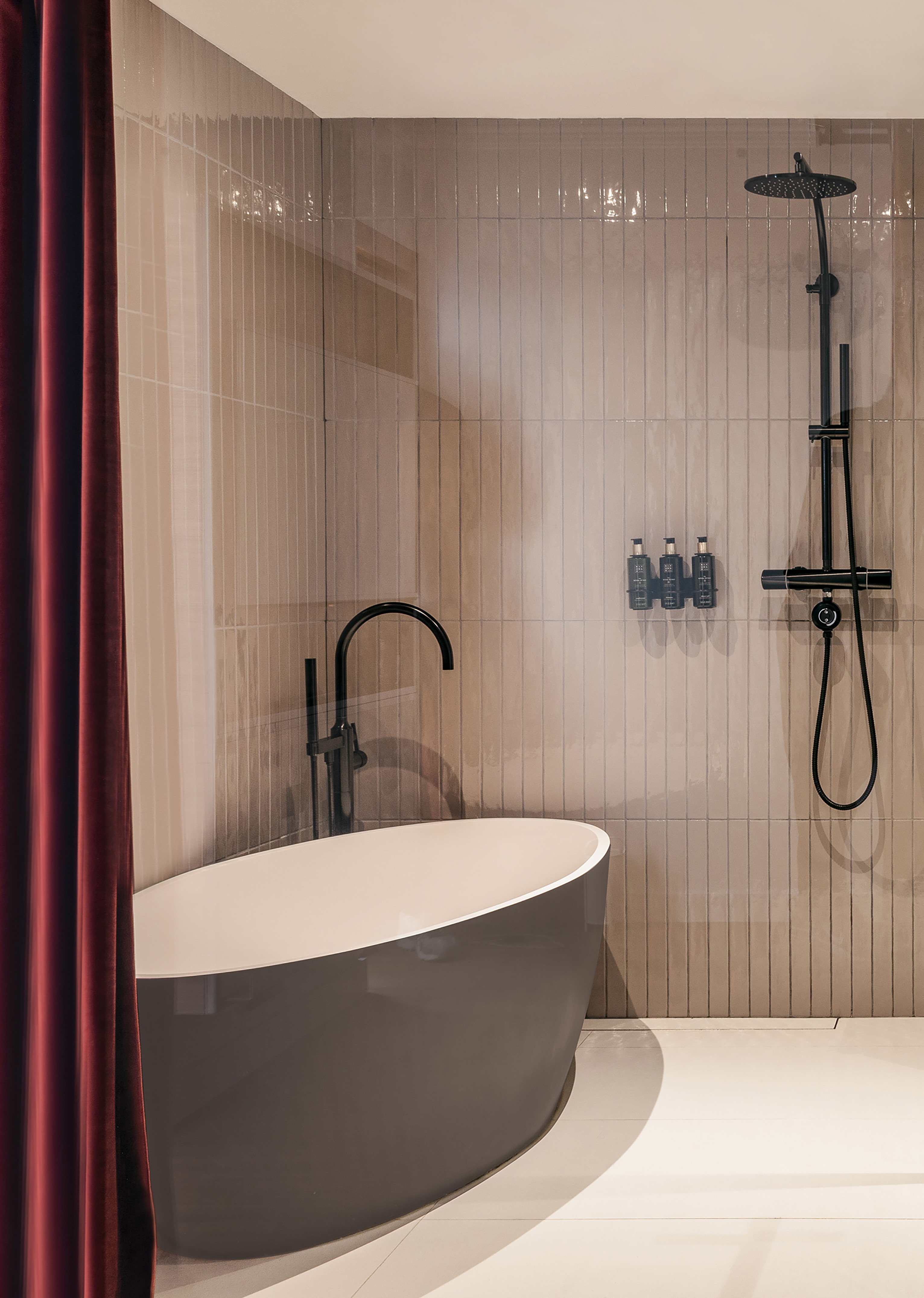Modern bathroom with freestanding tub, black shower, tiled wall, red curtain.