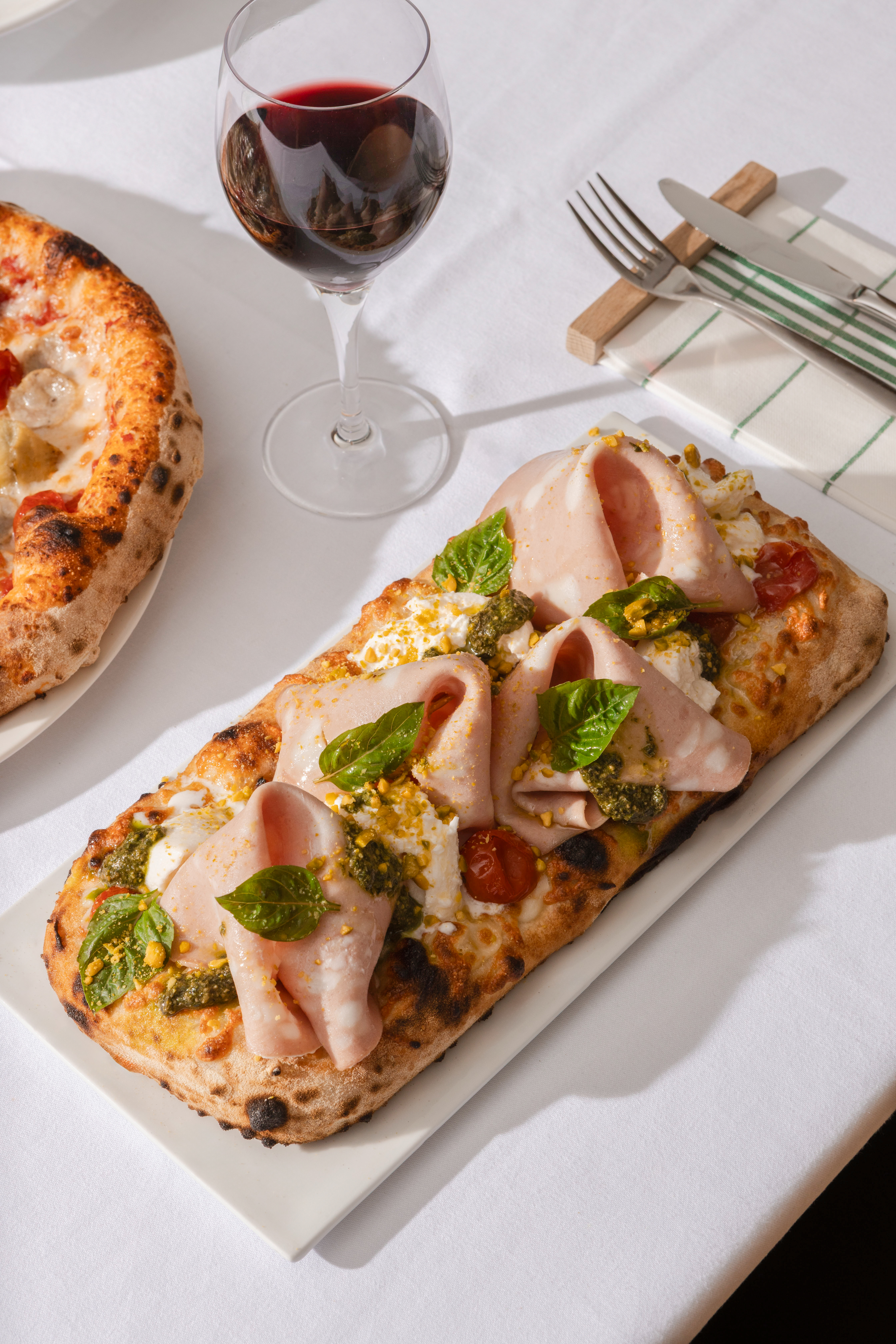 Mortadella pinsa with burrata, pesto, basil, pistachios and red wine.