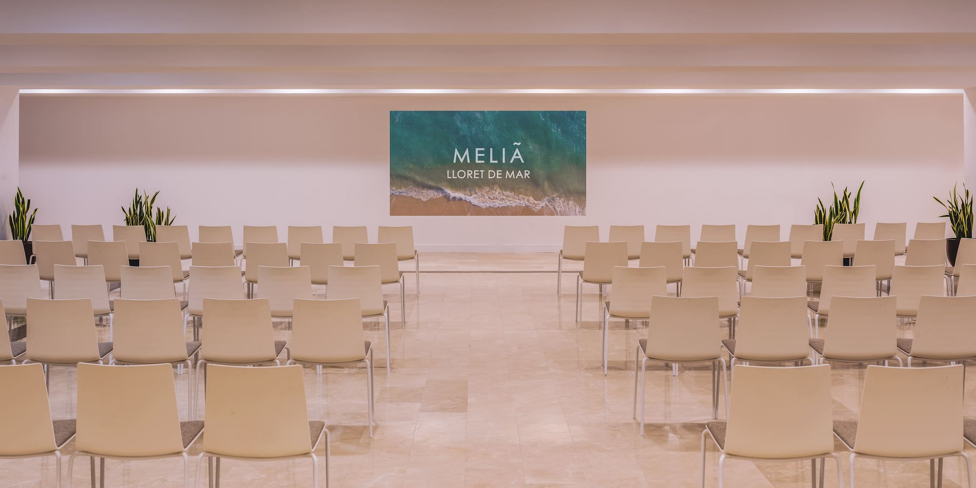 Hotel conference room with rows of empty chairs, Melia Lloret de Mar screen.
