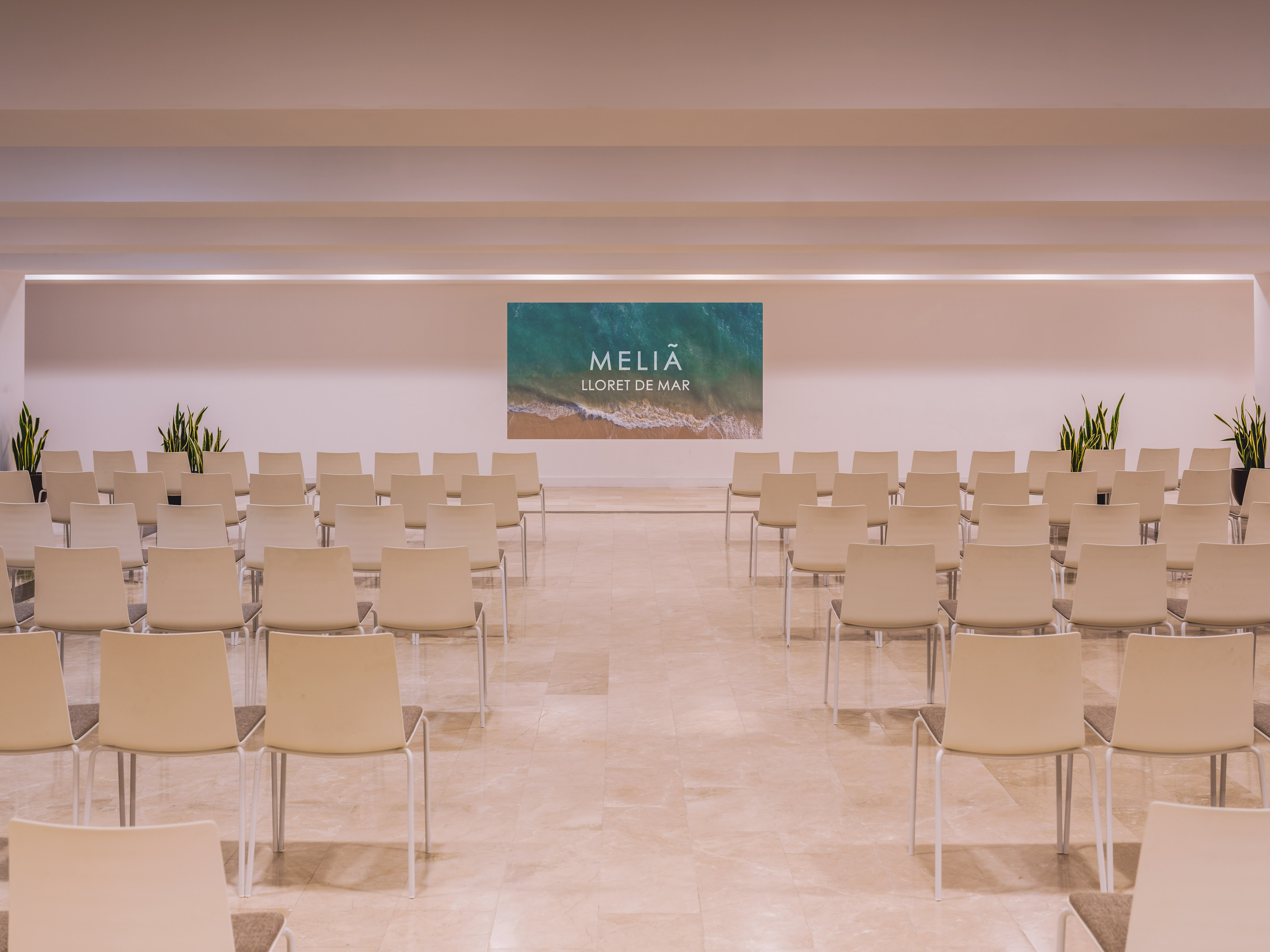 Hotel conference room with rows of empty chairs, Melia Lloret de Mar screen.