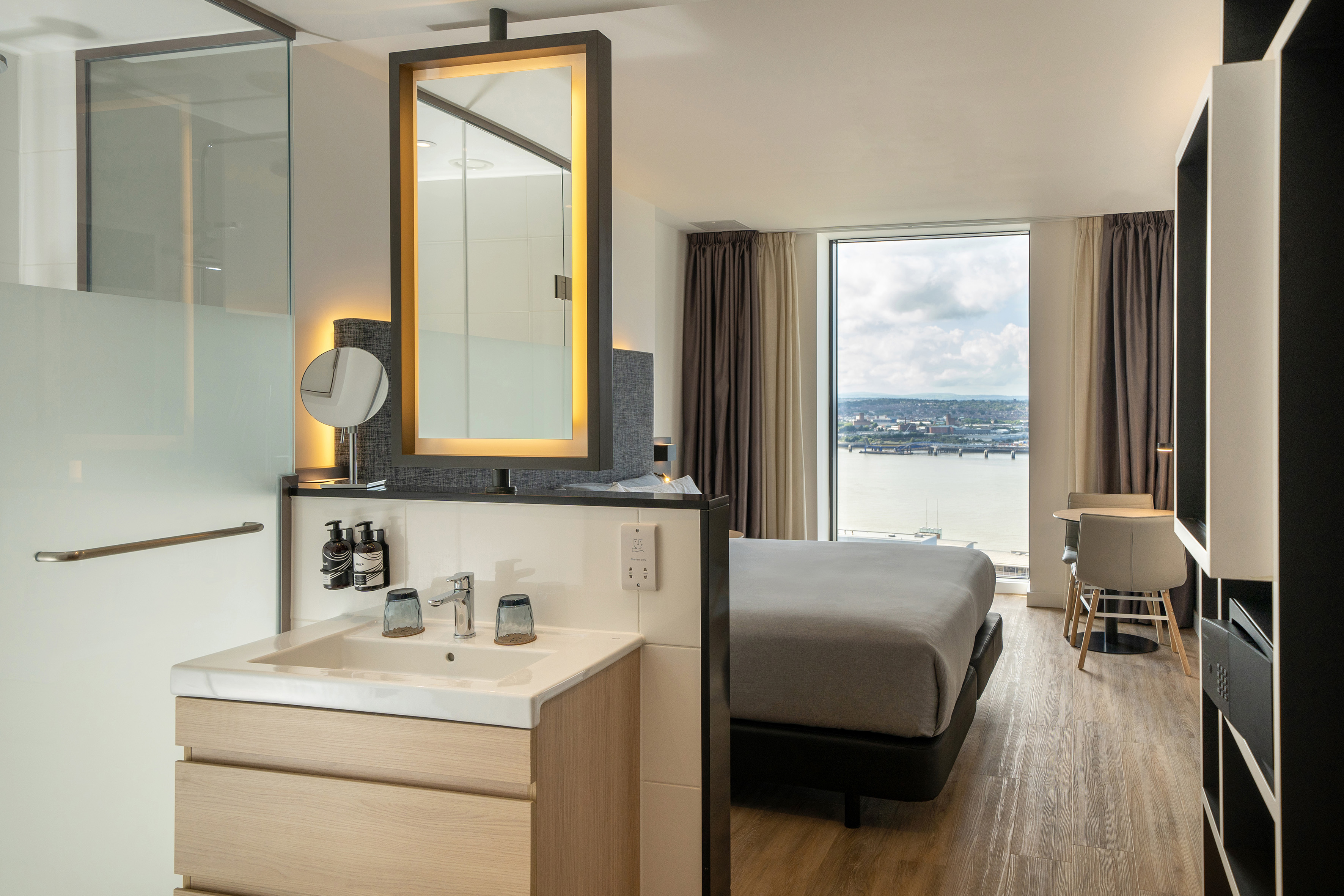 Contemporary hotel room with integrated bathroom, bed, and river view.