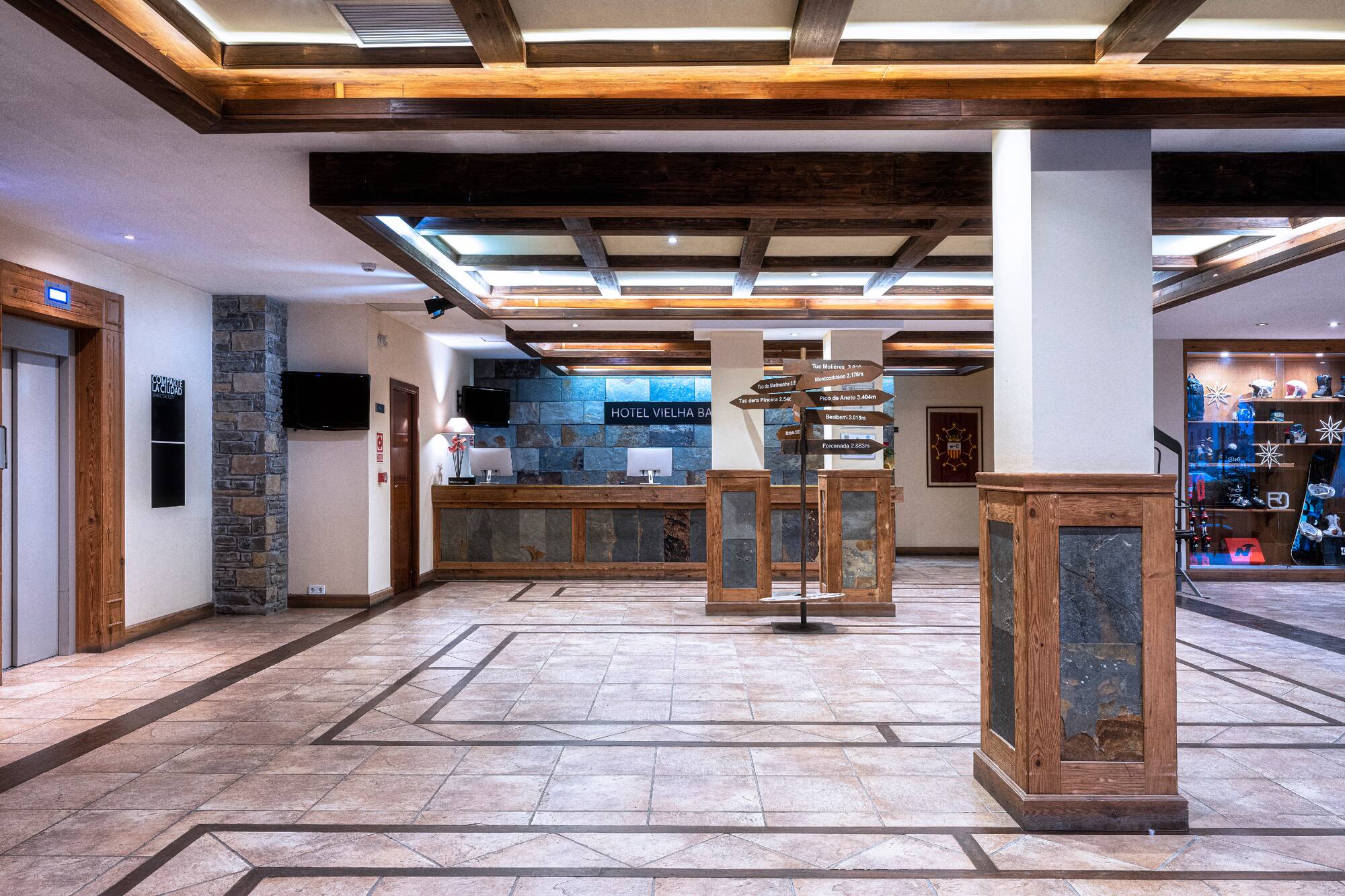 Vielha Baqueira lobby: rustic wood, stone, reception, and mountain sign.
