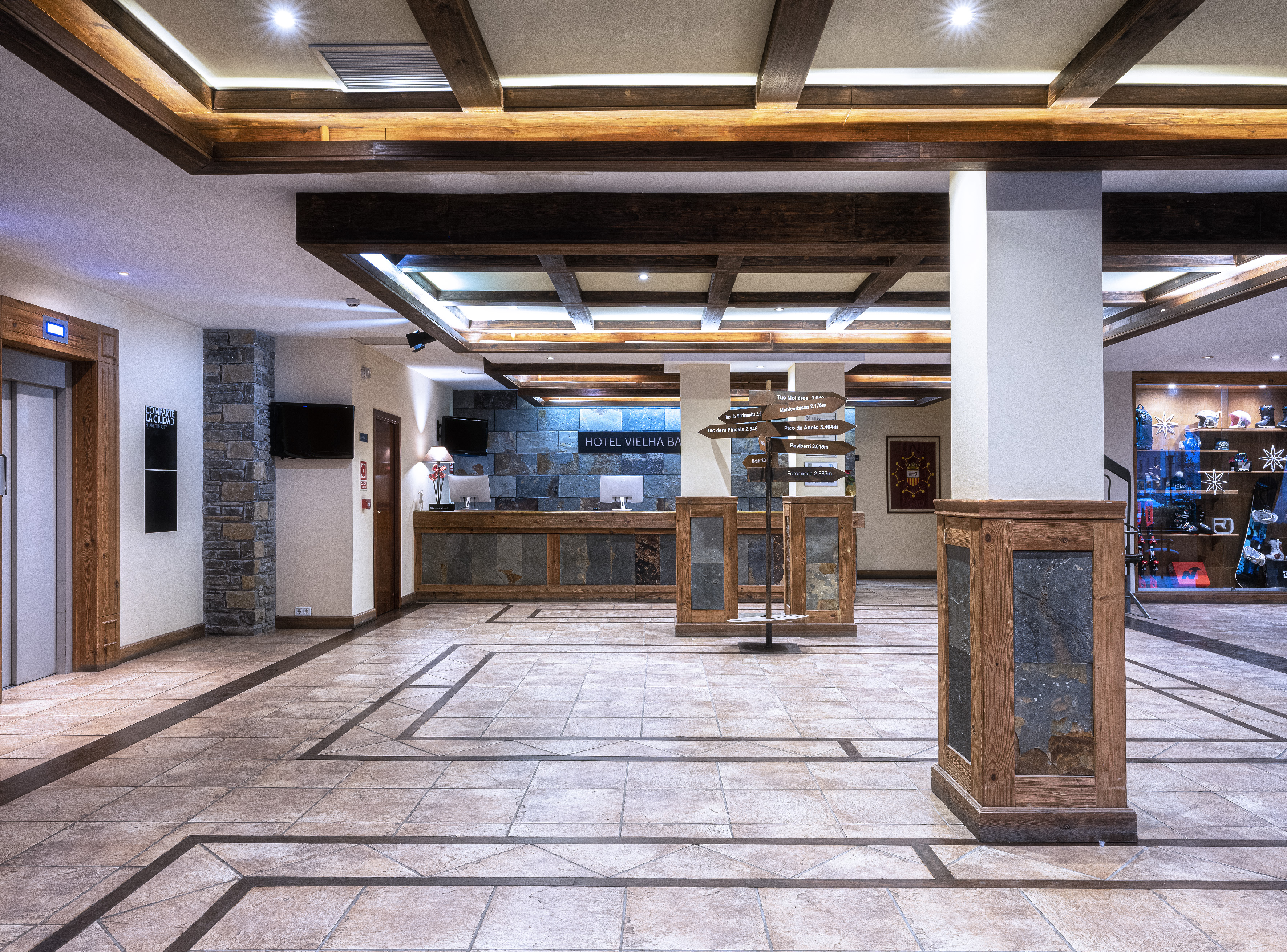 Vielha Baqueira lobby: rustic wood, stone, reception, and mountain sign.