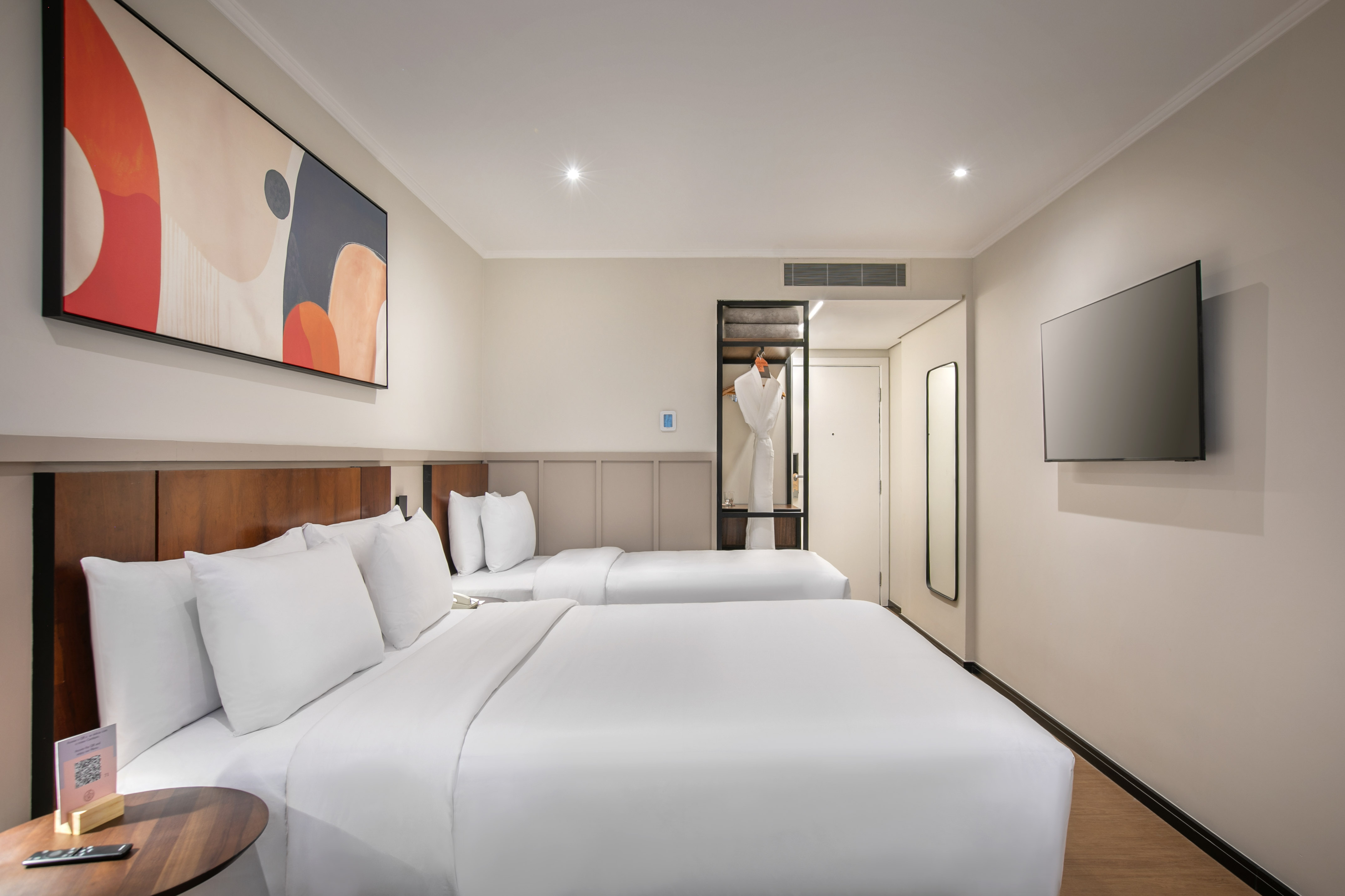 Modern hotel guest room with two beds, abstract art, TV, and open wardrobe.