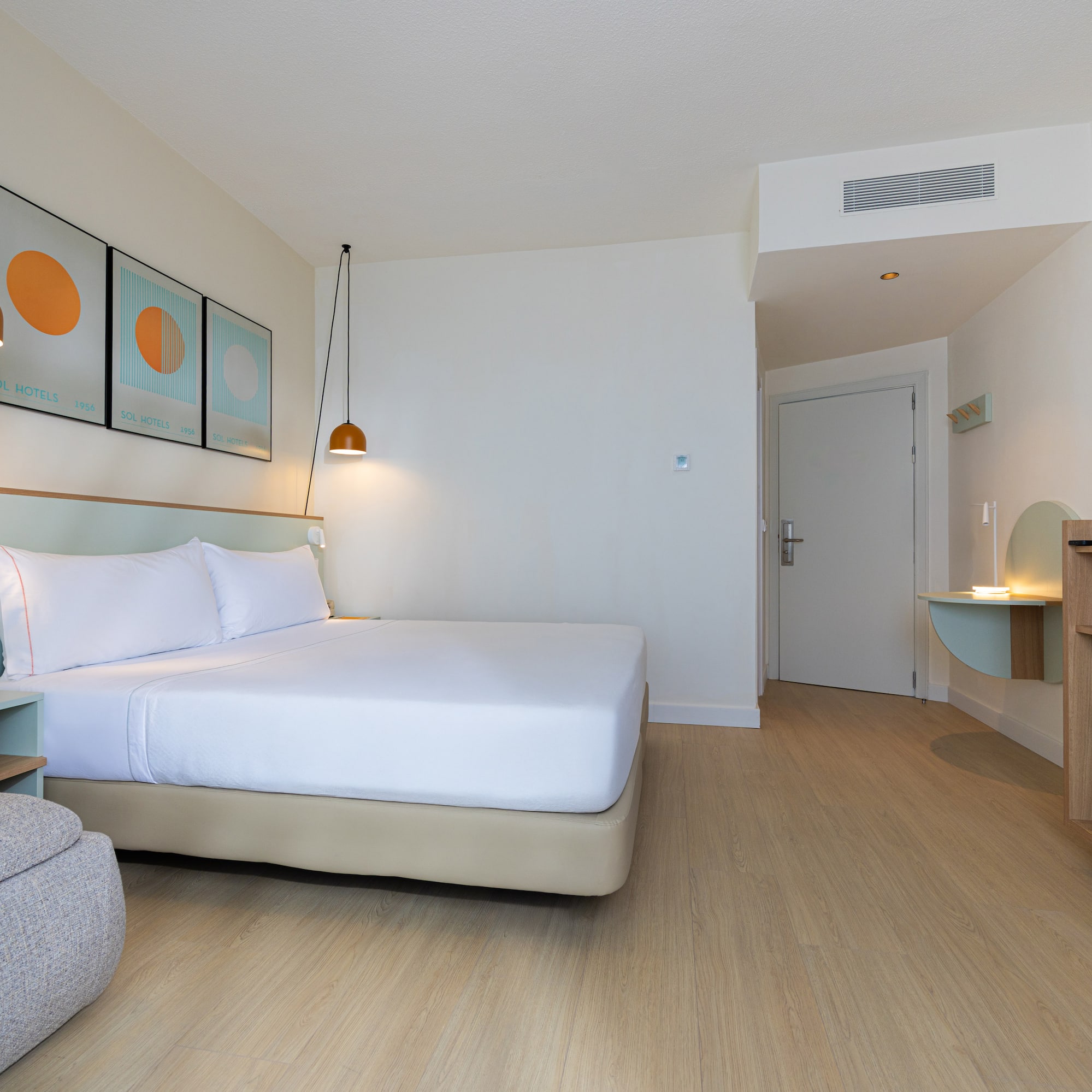 Modern hotel room with king bed, wood floor, mini-fridge, and TV.
