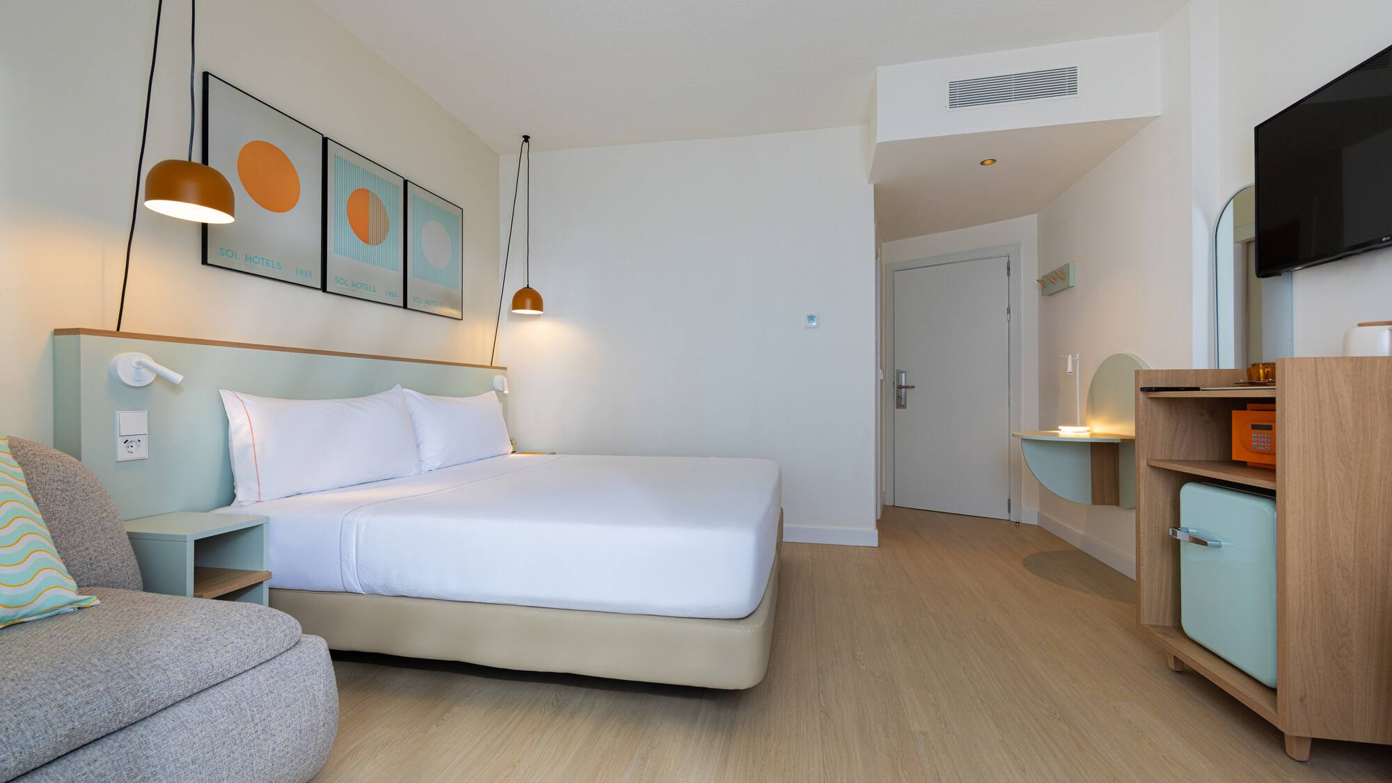 Modern hotel room with king bed, wood floor, mini-fridge, and TV.