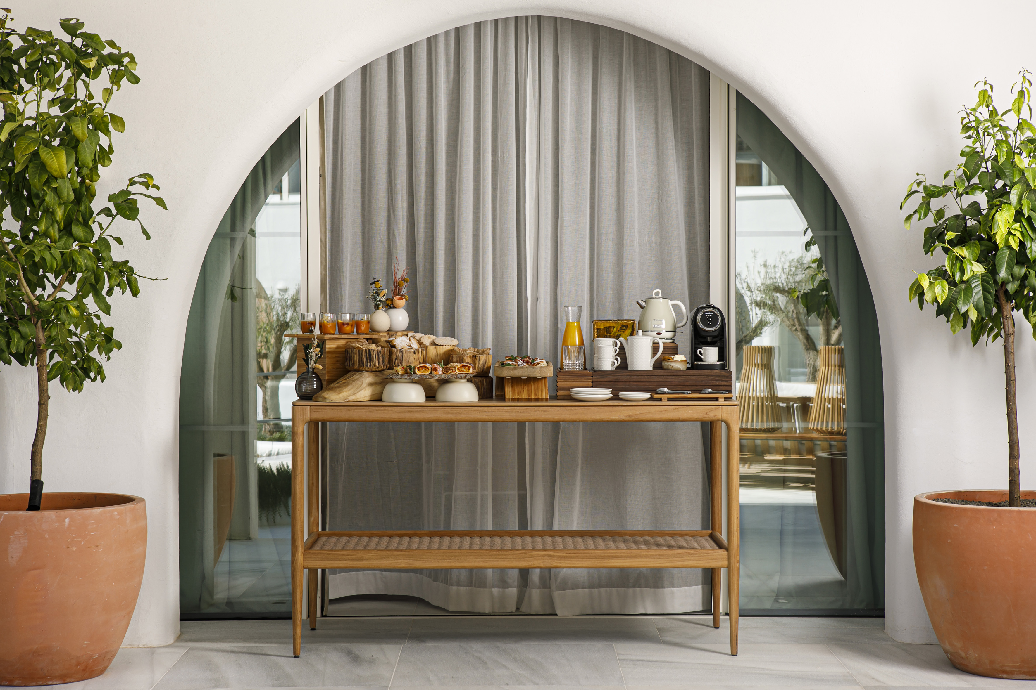 Hotel breakfast buffet with pastries, coffee, juice, arched outdoor patio.