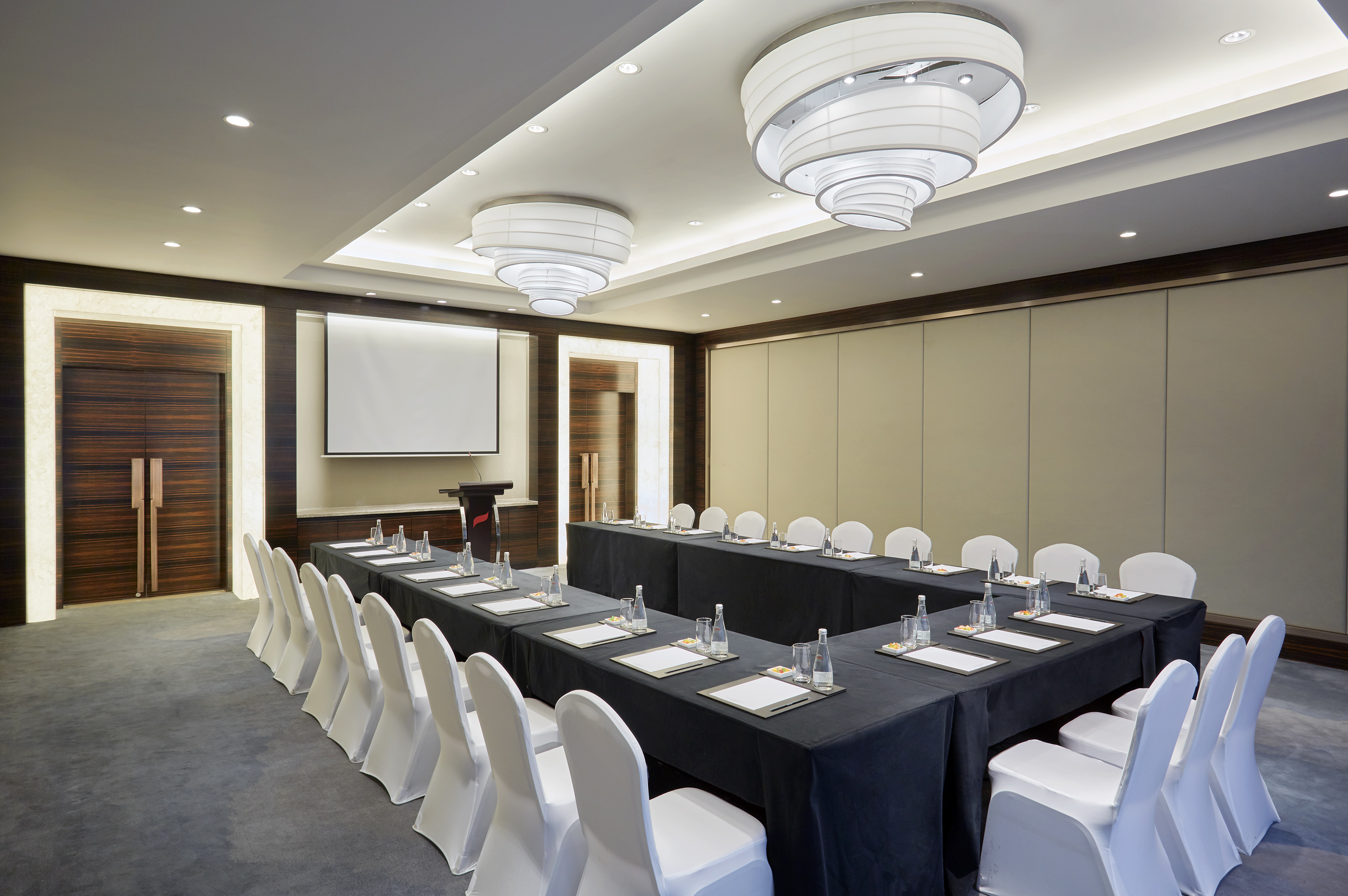 U-shape conference room with projection screen, white chairs, and black tables.