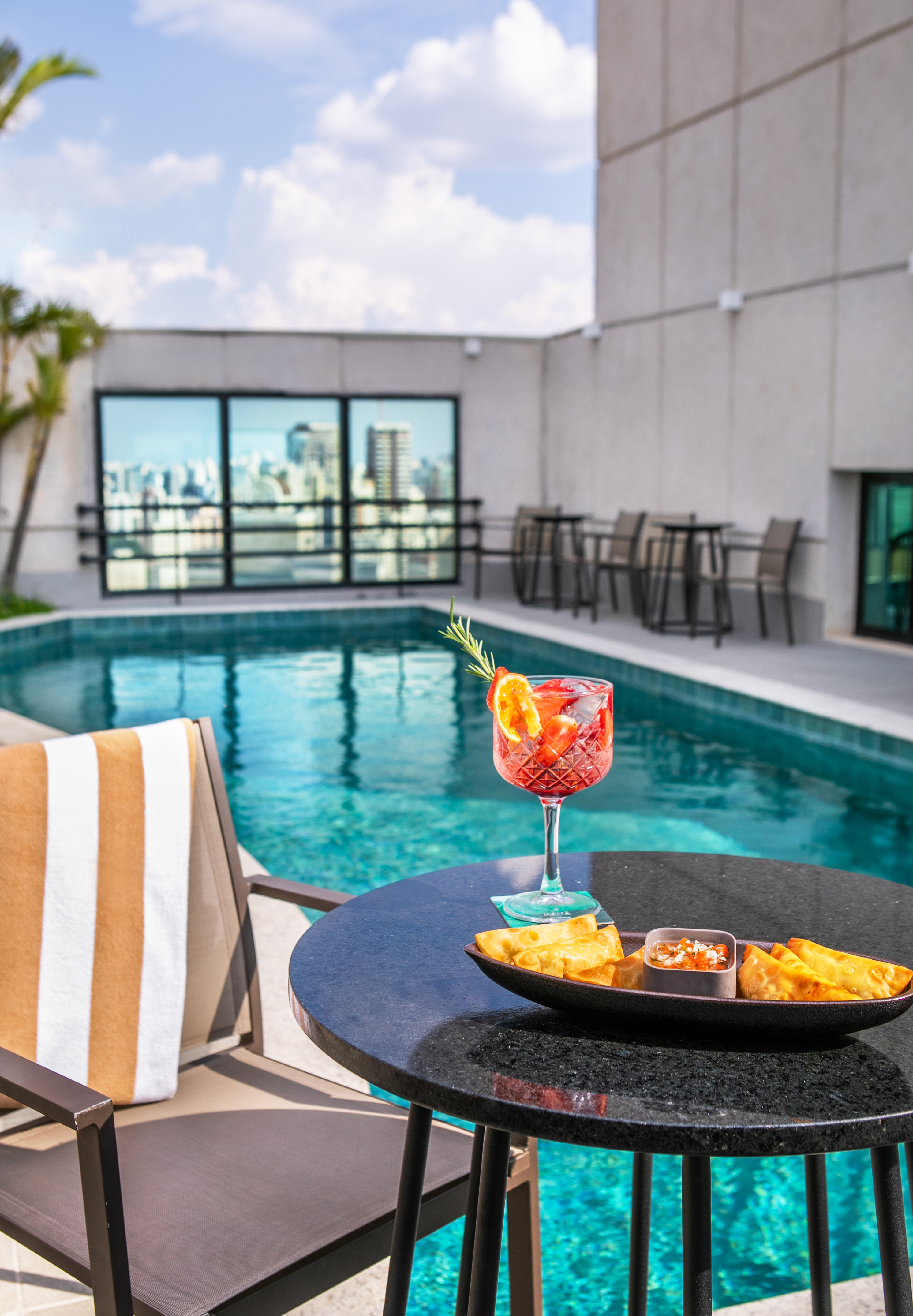 Cocktail and appetizers by rooftop pool with city skyline view.