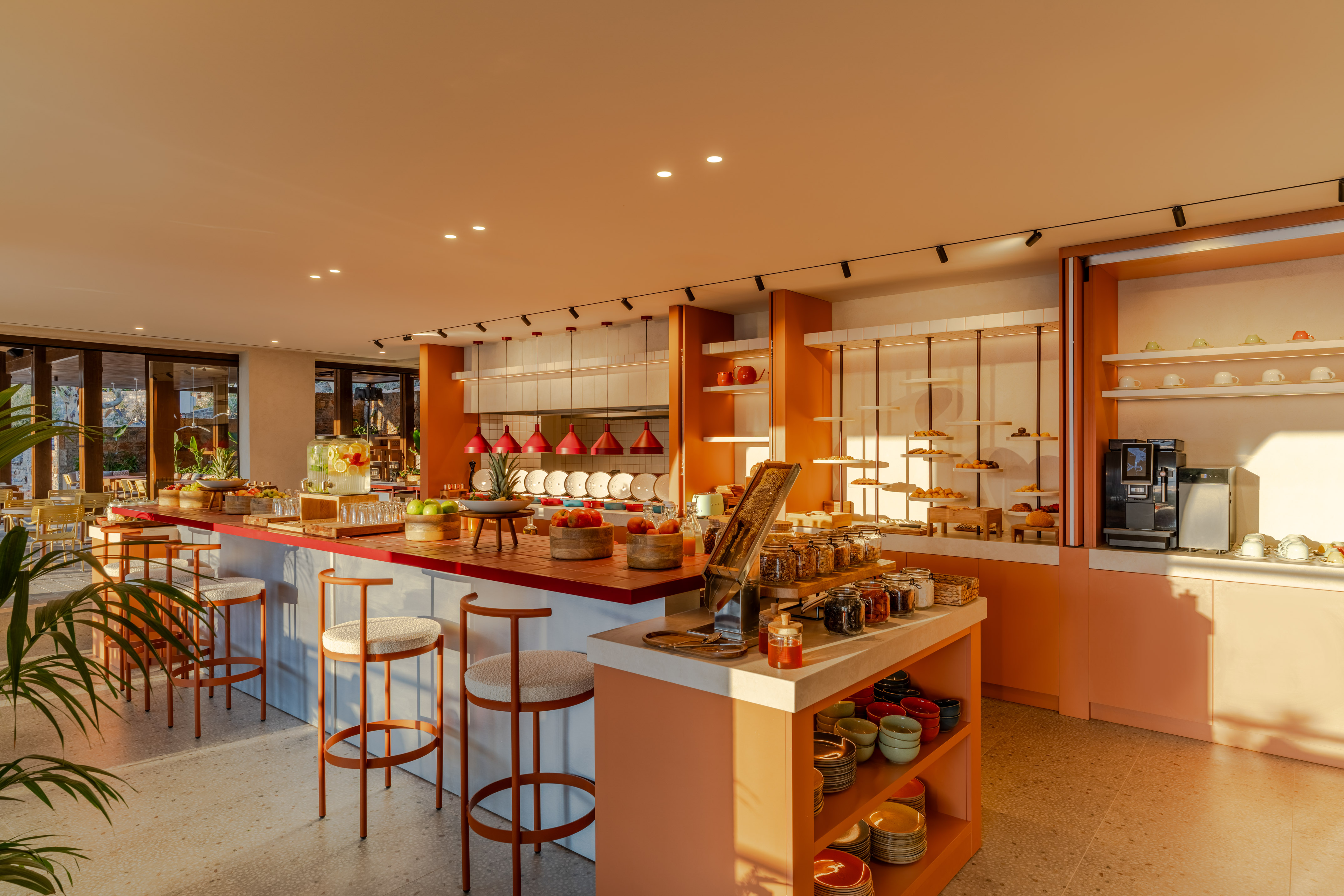 Warm modern hotel breakfast buffet, fruits, pastries, coffee, bar stools.