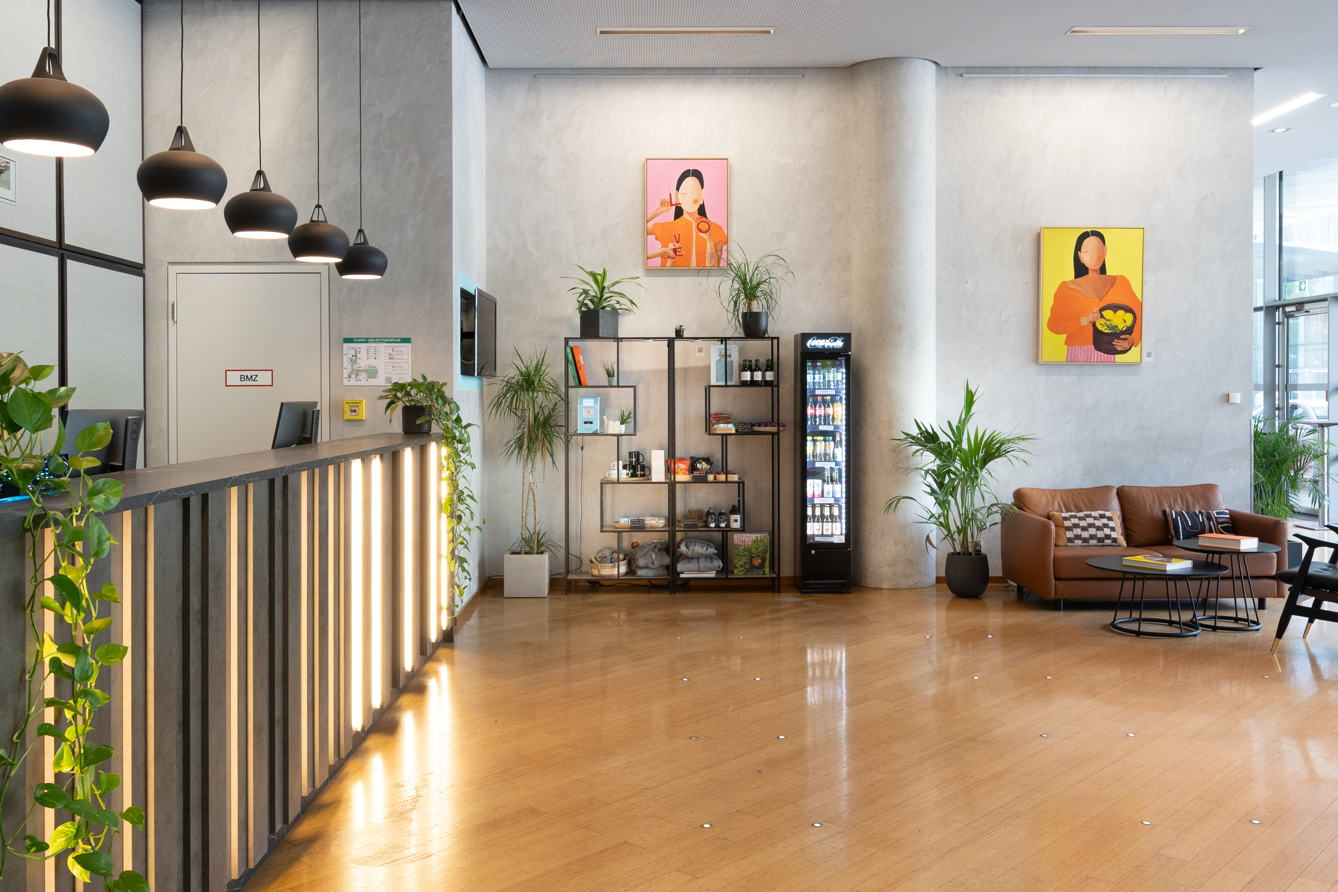 Contemporary office lobby with reception desk, lounge, colorful art, and plants.