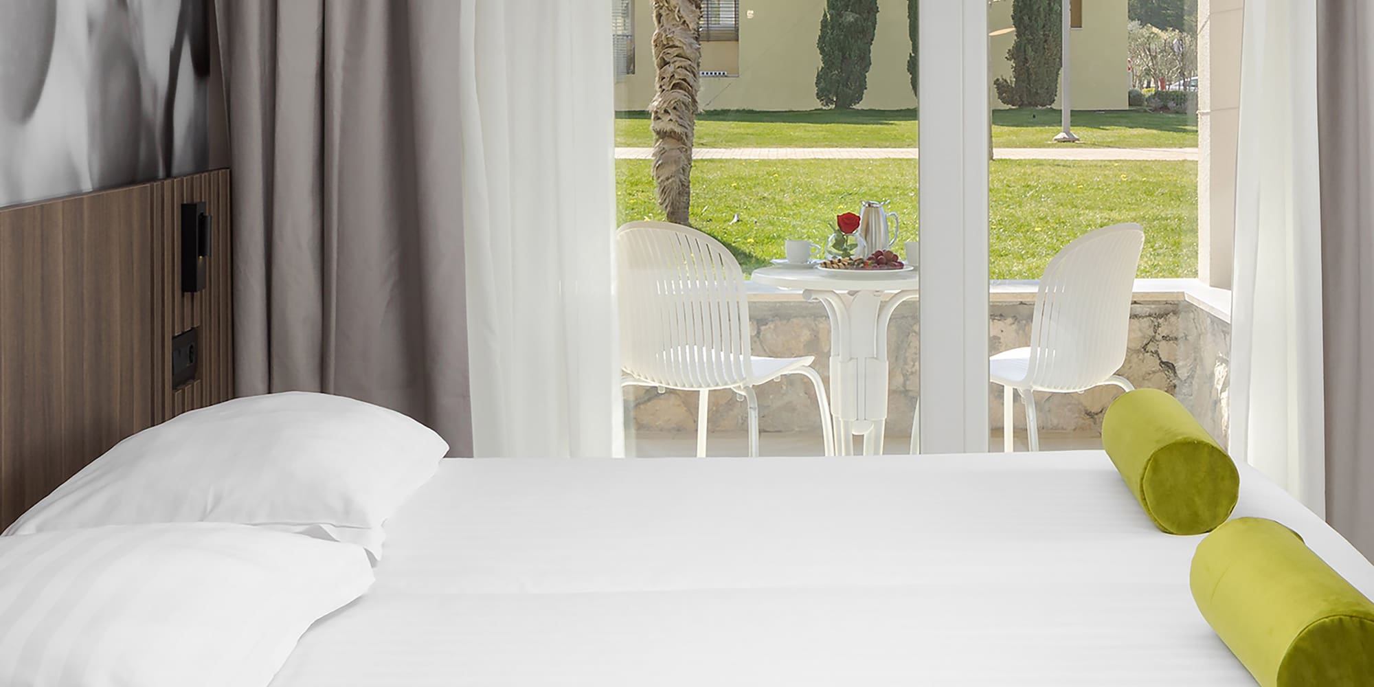 a bed with white sheets and green pillows in a room with a glass door