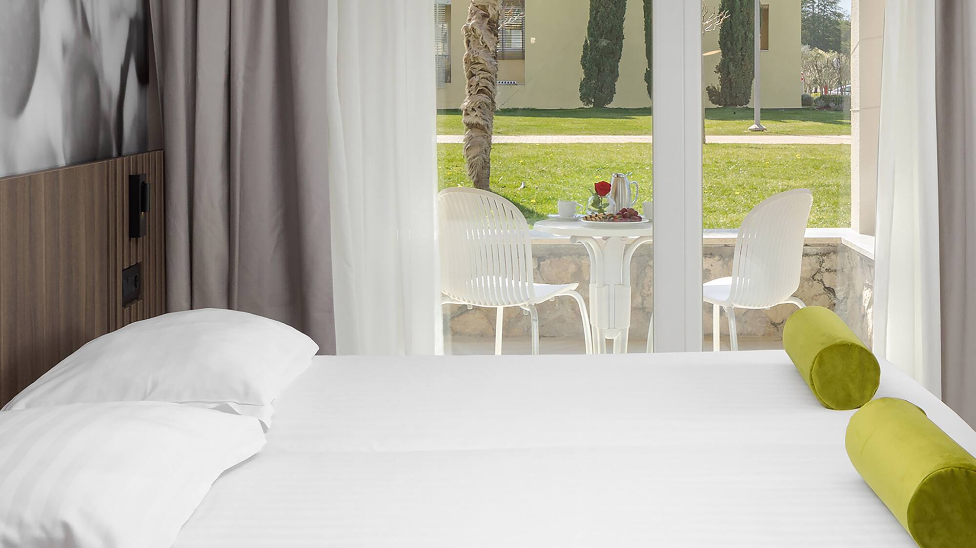 a bed with white sheets and green pillows in a room with a glass door