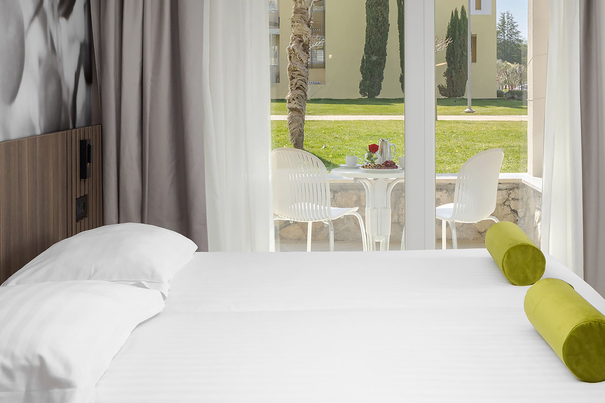 a bed with white sheets and green pillows in a room with a glass door