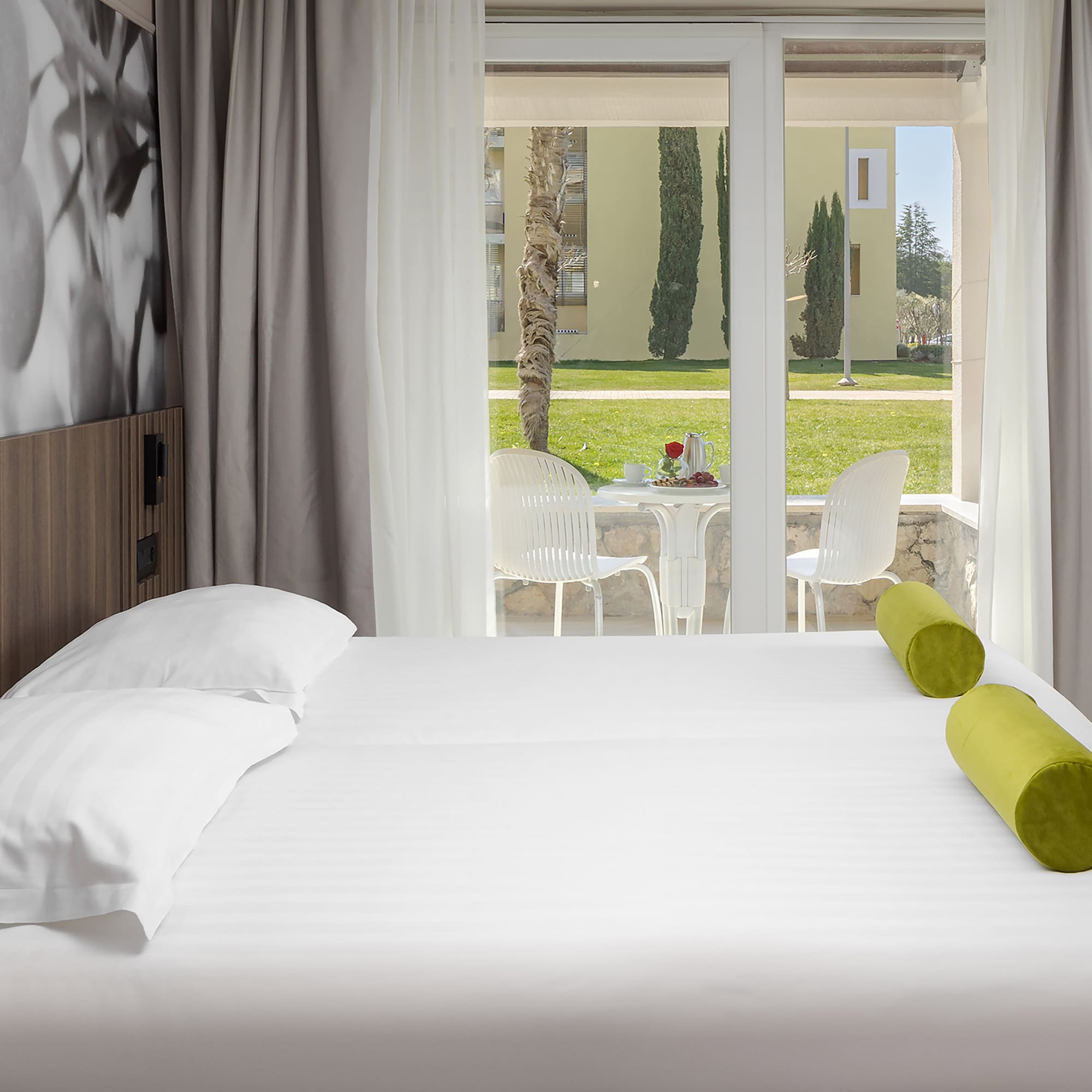 a bed with white sheets and green pillows in a room with a glass door