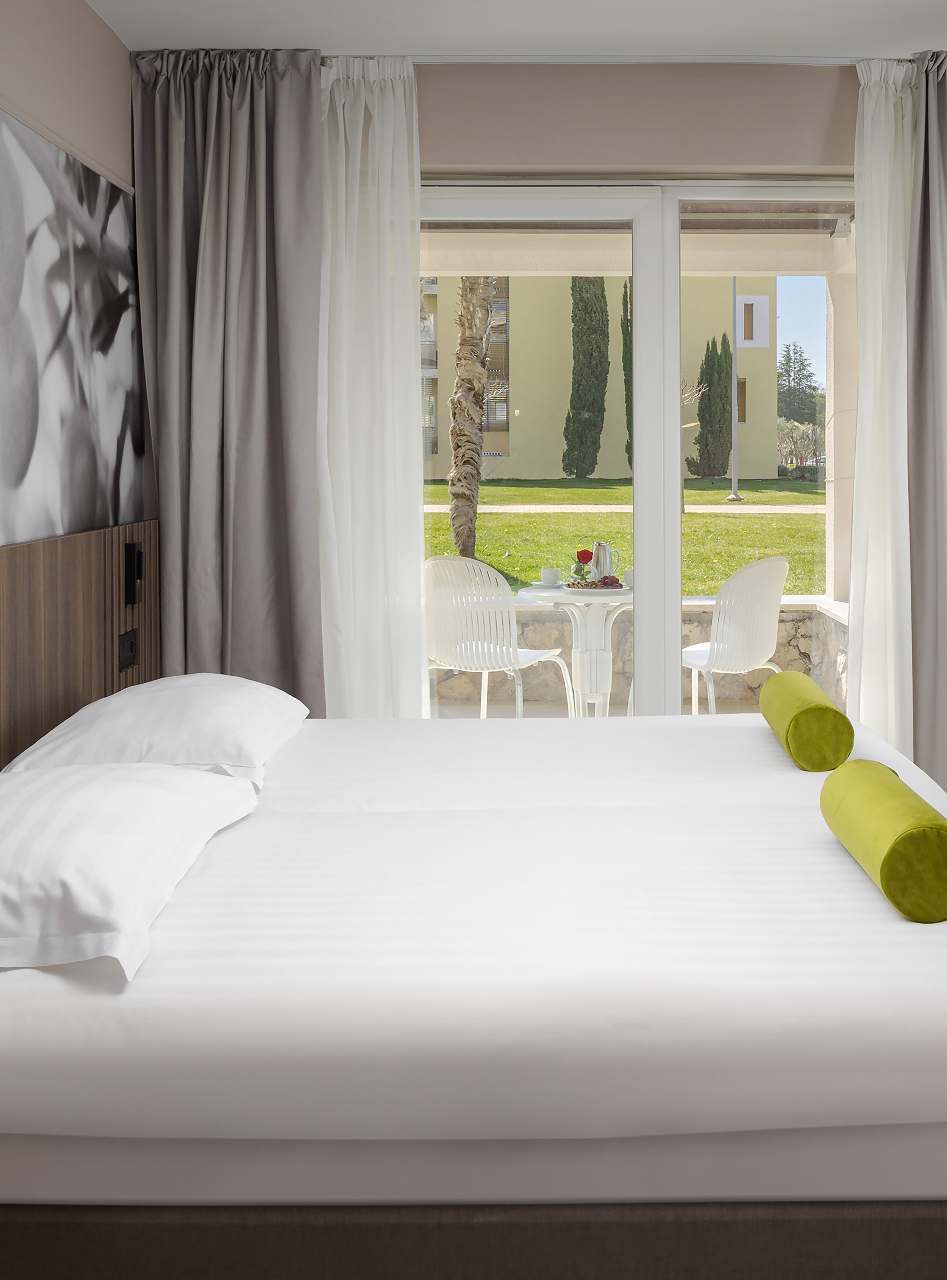 a bed with white sheets and green pillows in a room with a glass door